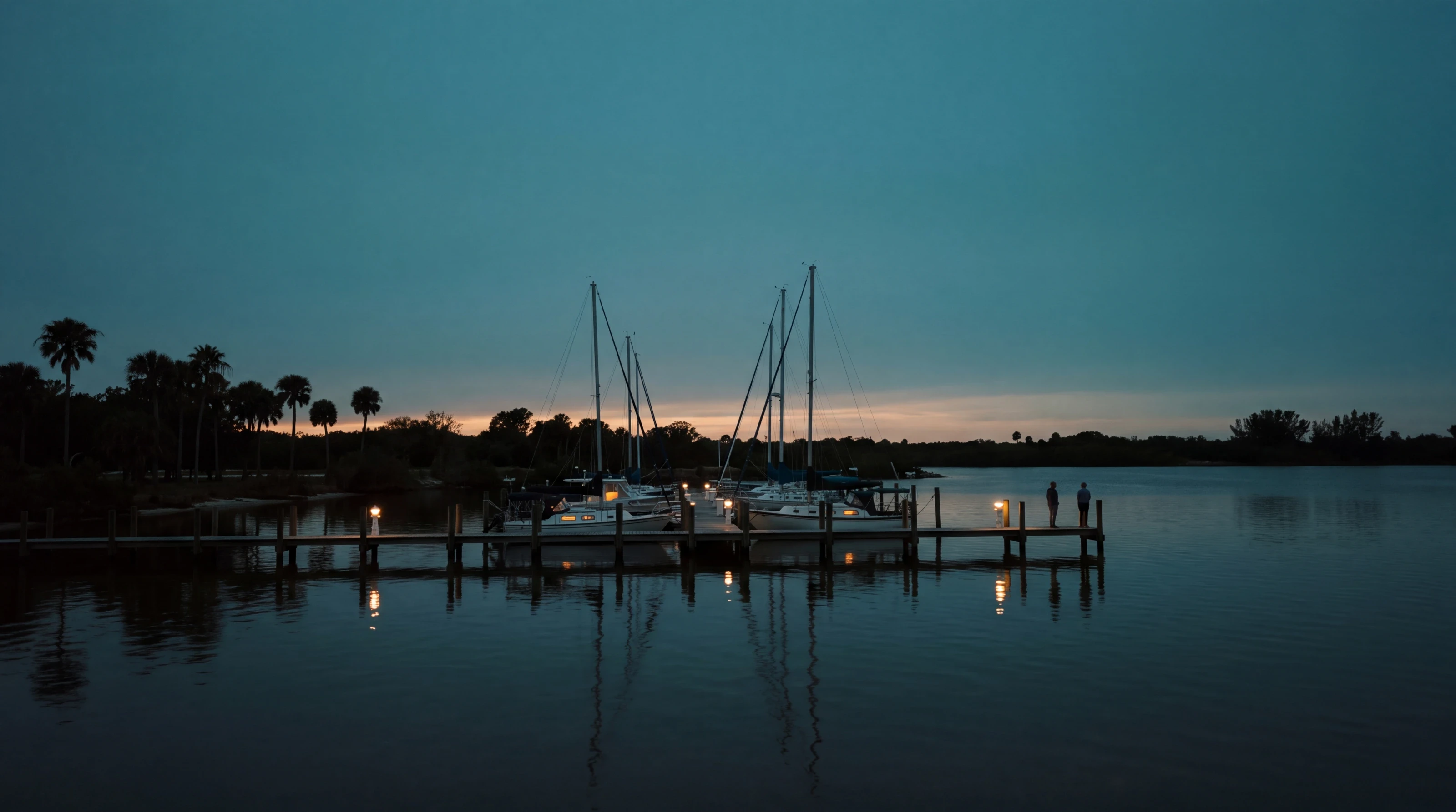 Sailboats and a lamp-lit dock at a small Florida marina at dusk