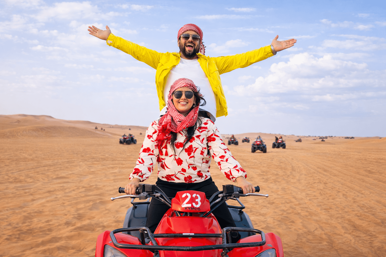 Couple riding a red quad bike in the Dubai desert with other riders in the background during a desert safari adventure