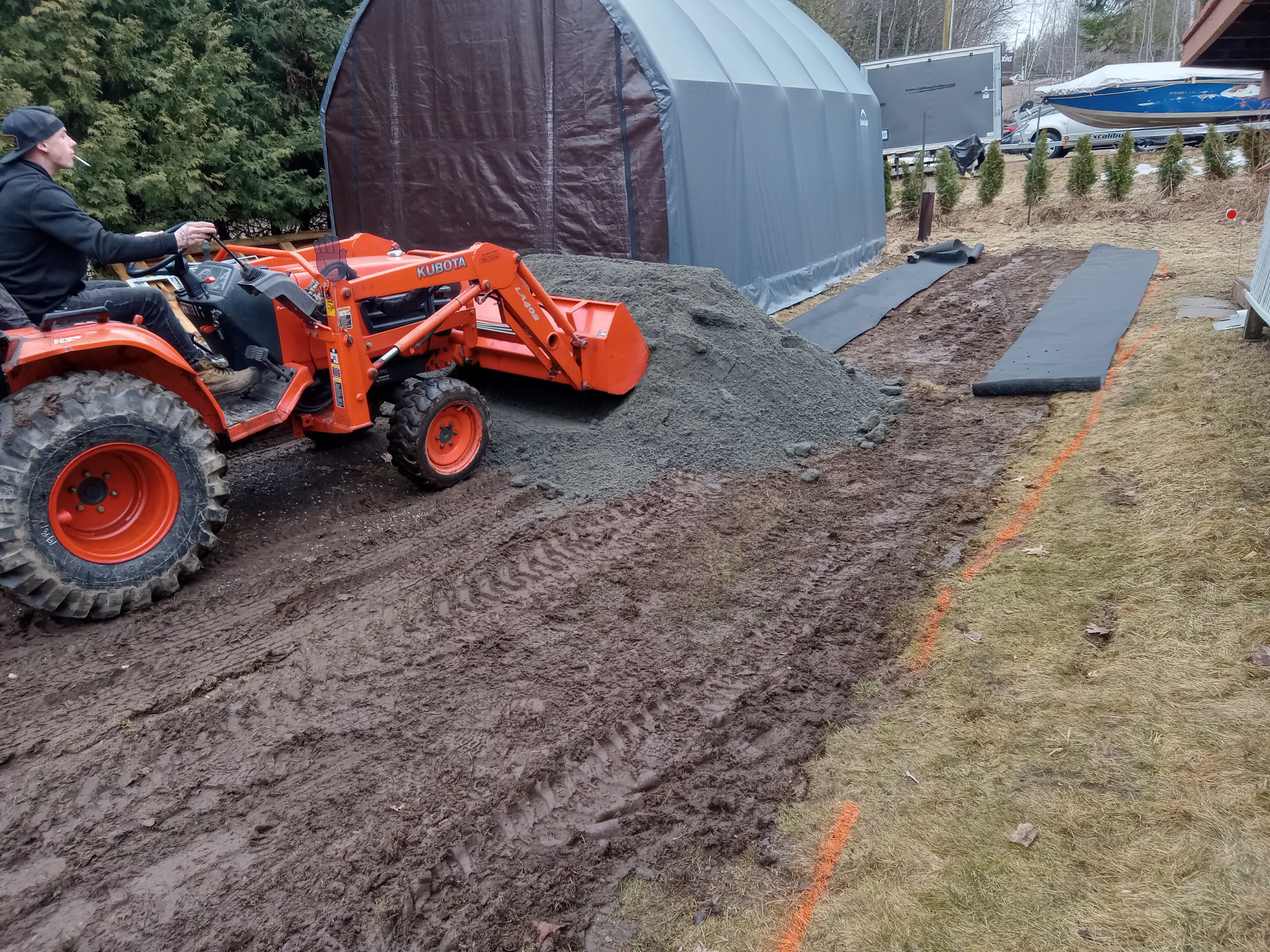 Gravel driveway and parking area under construction beside a storage shelter.