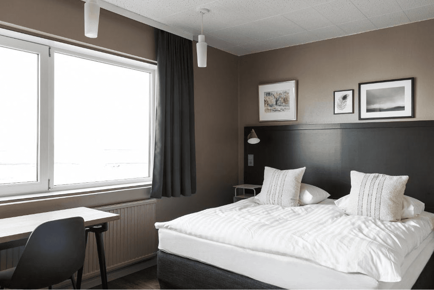 Hotel bedroom with wooden furniture, a comfortable bed, a small workspace, and soft natural light
