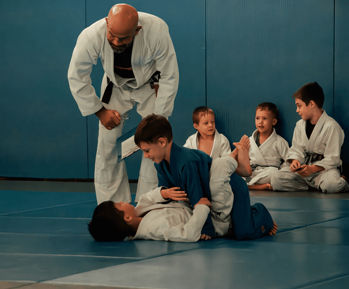 Group of children on the mat smiling and learning Jiu Jitsu together