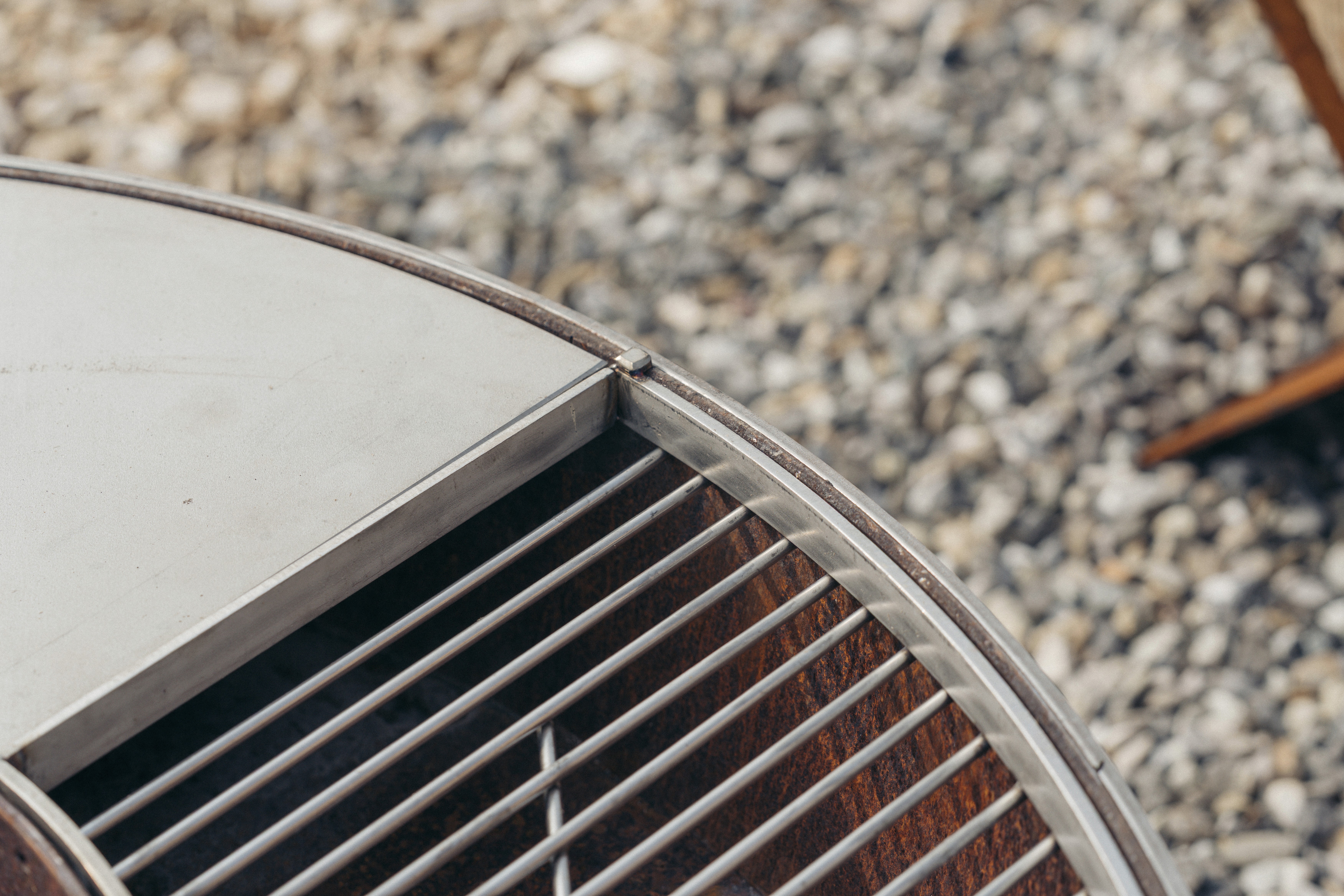 Nahaufnahme einer metallischen Grillfläche mit runden und rechteckigen Grillbereichen und einer rustikalen, strukturierten Oberfläche.