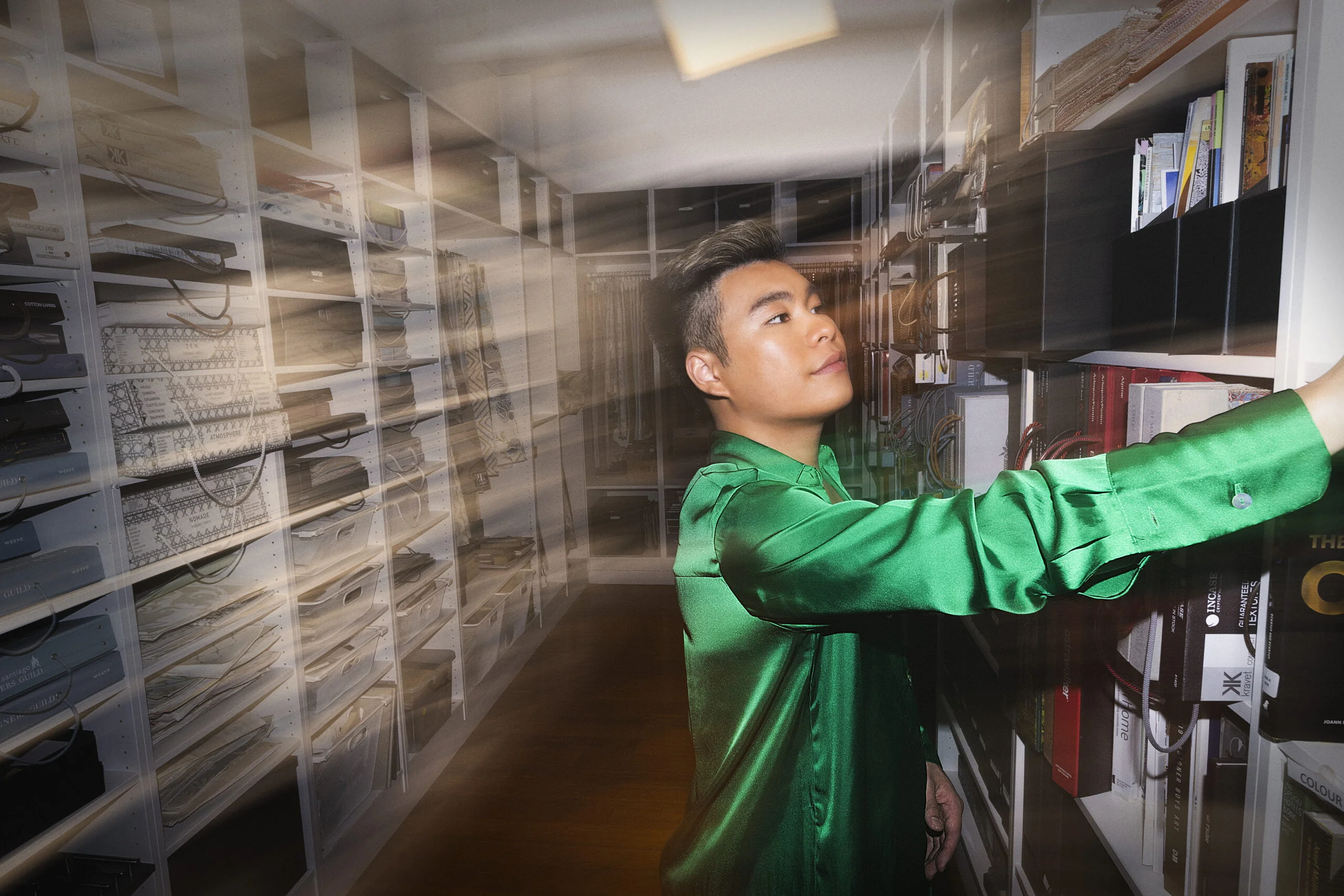 Man in a green satin shirt reaching for a shelf in a light-streaked storeroom, from Collarts' 'Creativity can't wait'