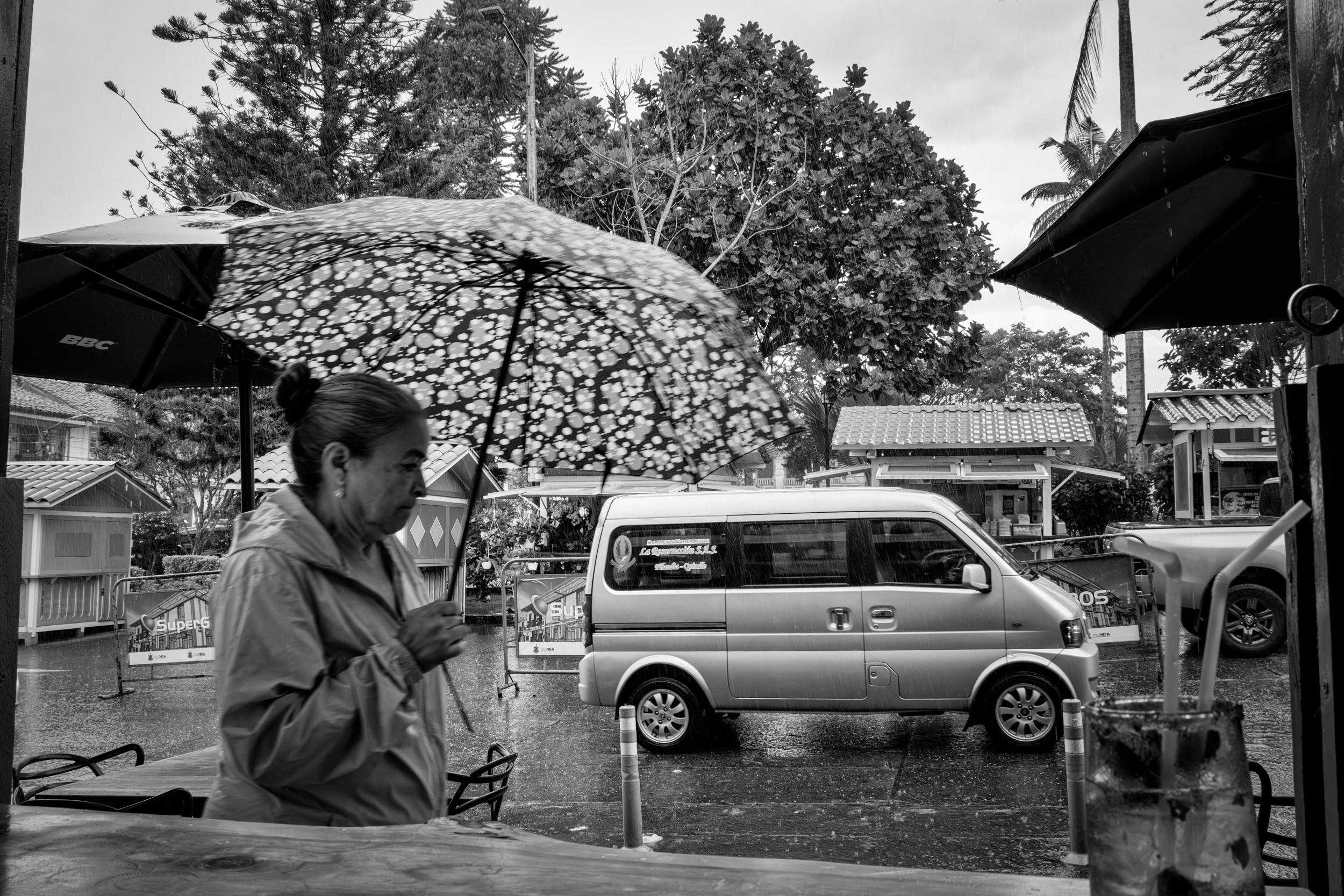 Rainy street scene with people passing by a bar window.