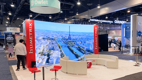 20x20 trade show booth with branded wall graphics, reception counter, seating area, lighting, and island booth layout