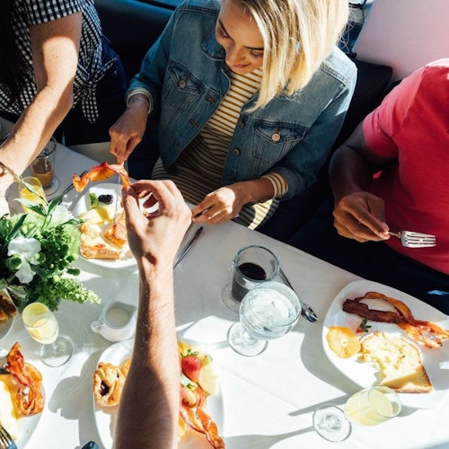 Three people eating breakfast at a table with plates of food, including bacon and eggs, and beverages like coffee and water.