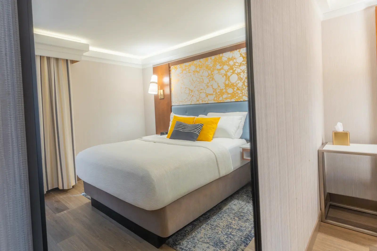 Modern hotel room with a desk, bright yellow chair, and wall-mounted TV.