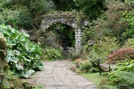 Secret garden stone archway surrounded by lush greenery and ferns with winding path leading through ruins