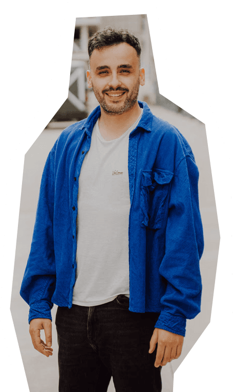 Portrait d'un homme souriant portant une chemise bleue et un t-shirt blanc sur fond extérieur flou.