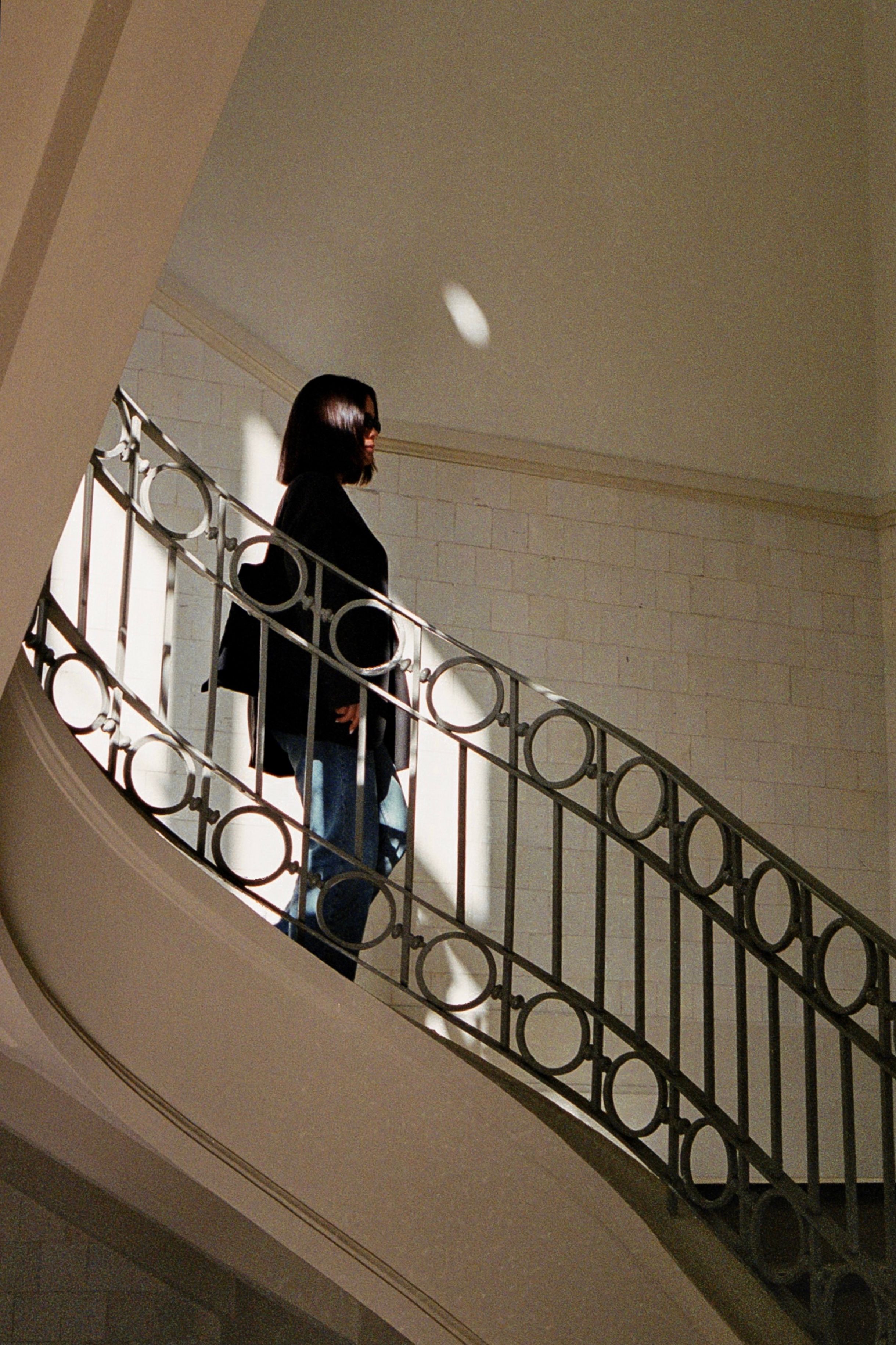A woman walks up a sweeping curved staircase with an ornate metal railing inside a museum.