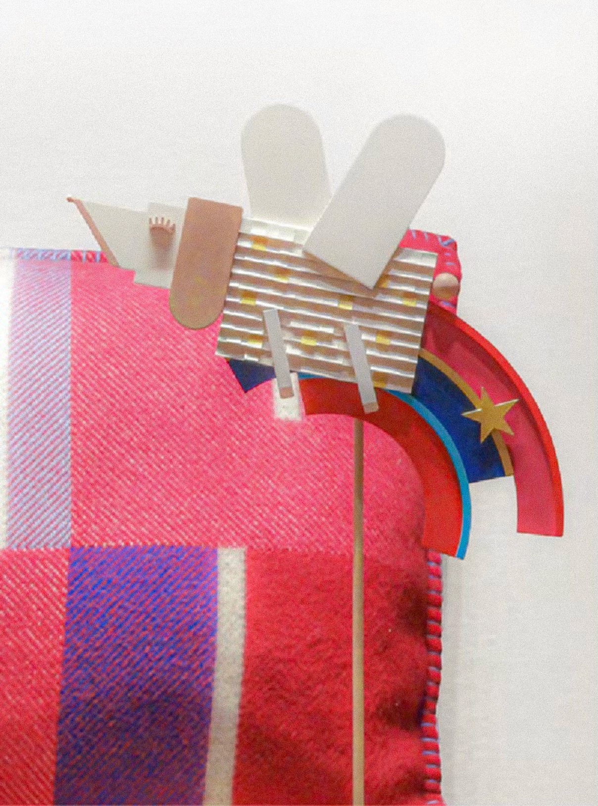 In-store holiday decor for Hermès featuring a stylized white wooden dog character with a rainbow and star accessory, placed against a vibrant red and pink patterned textile background, designed by WM Paris.