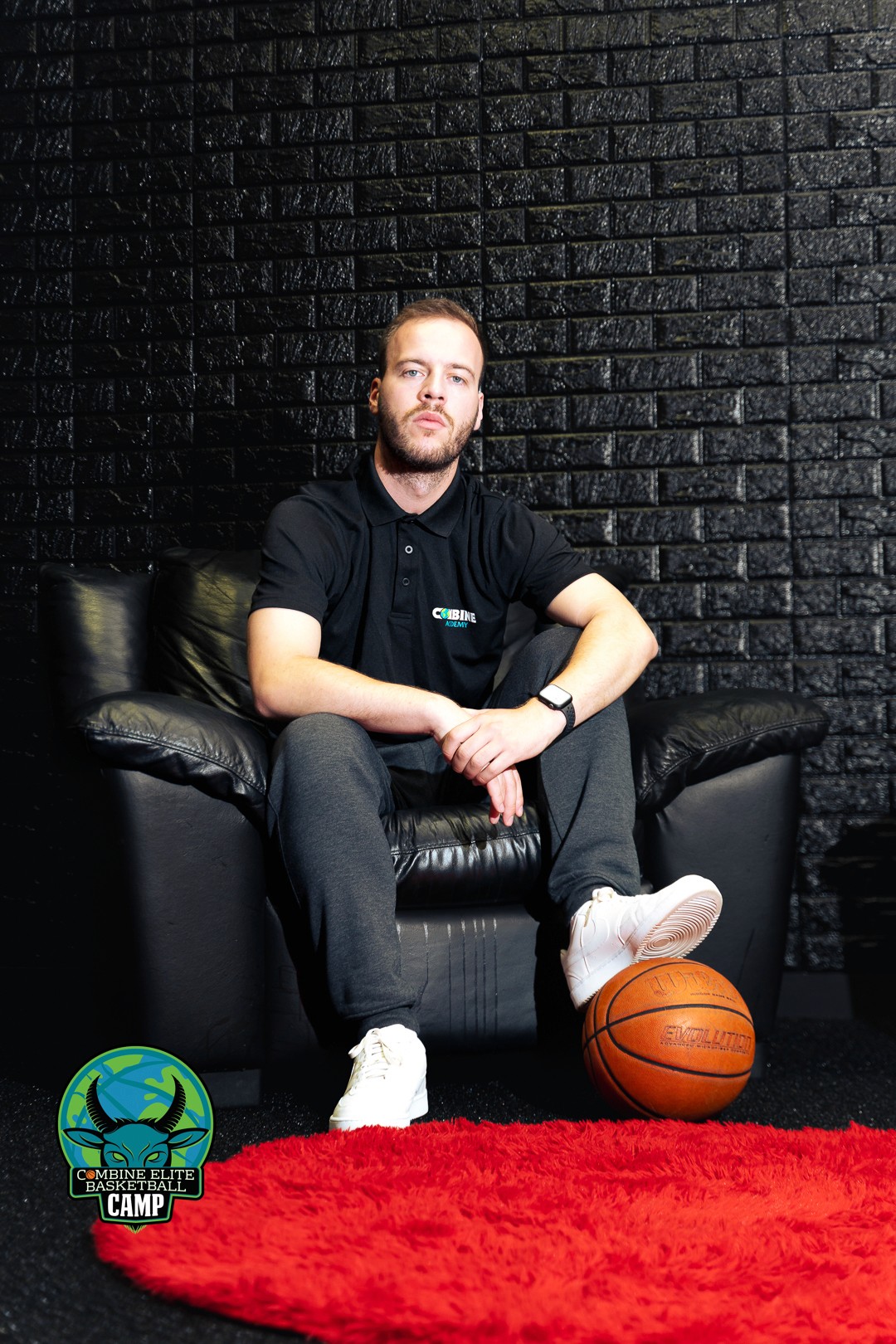 Entraîneur assis sur un fauteuil, ballon posé au pied.  