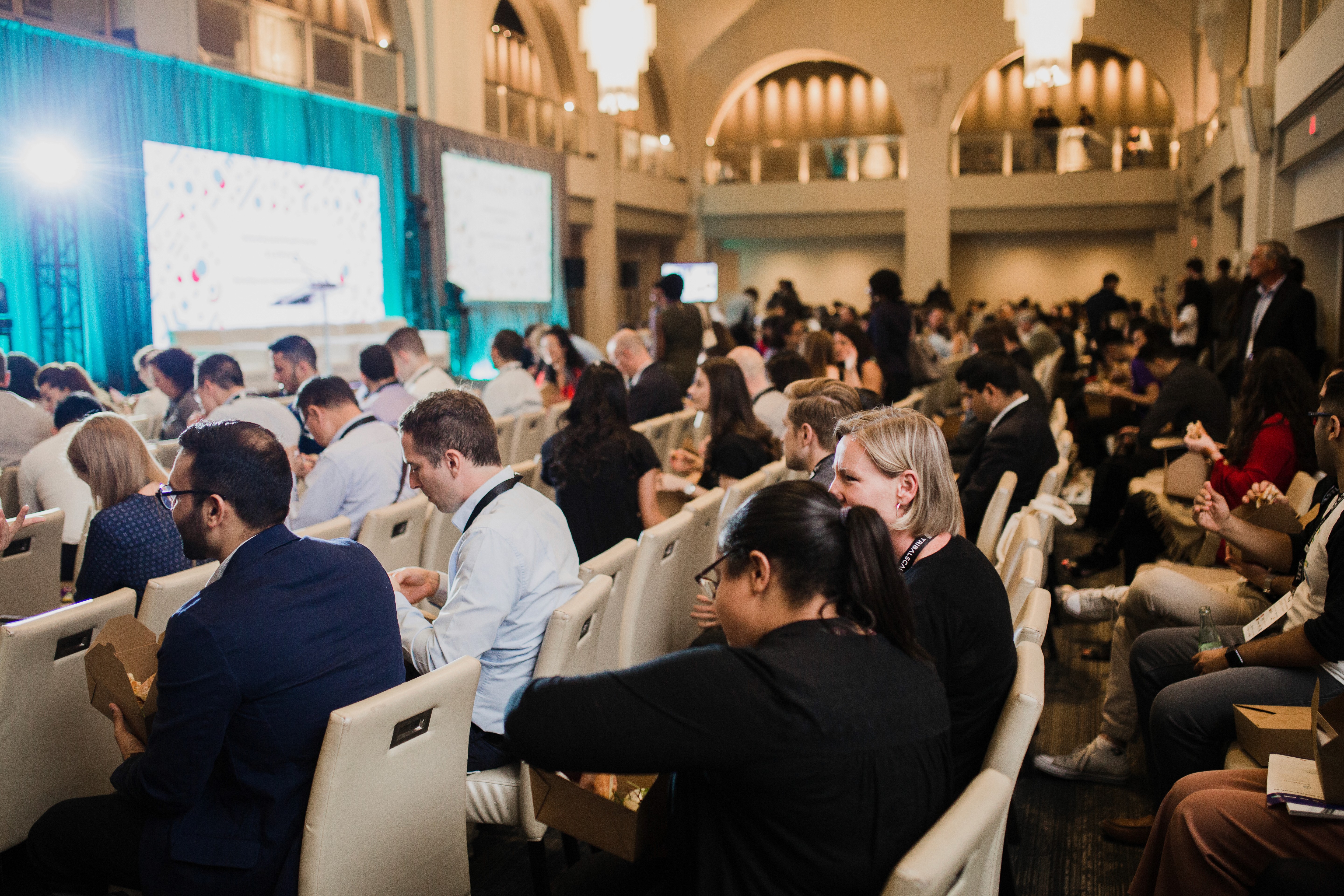 A room of people watching a keynote speaker in a large event hall