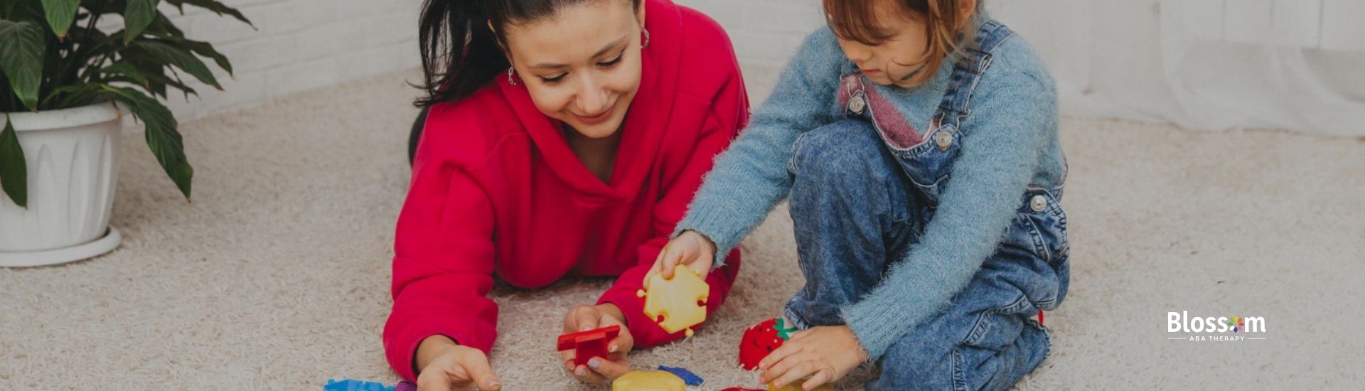 An ABA therapist and a girl playing with colorful building blocks on a carpeted floor.