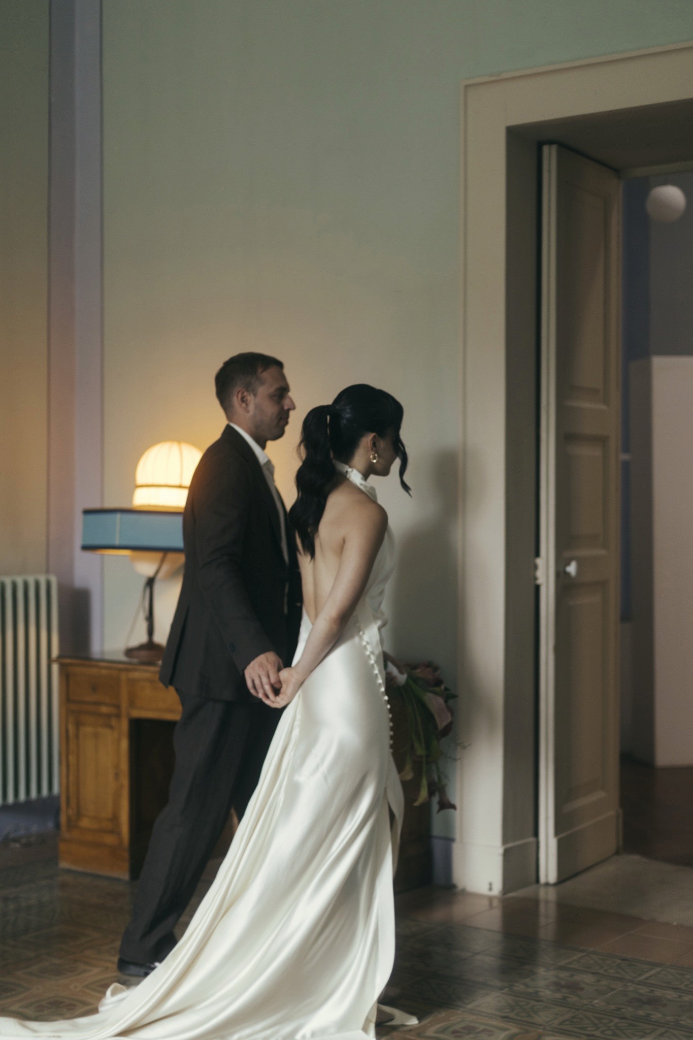 Toey and Otto walking hand in hand through a warm-lit villa room