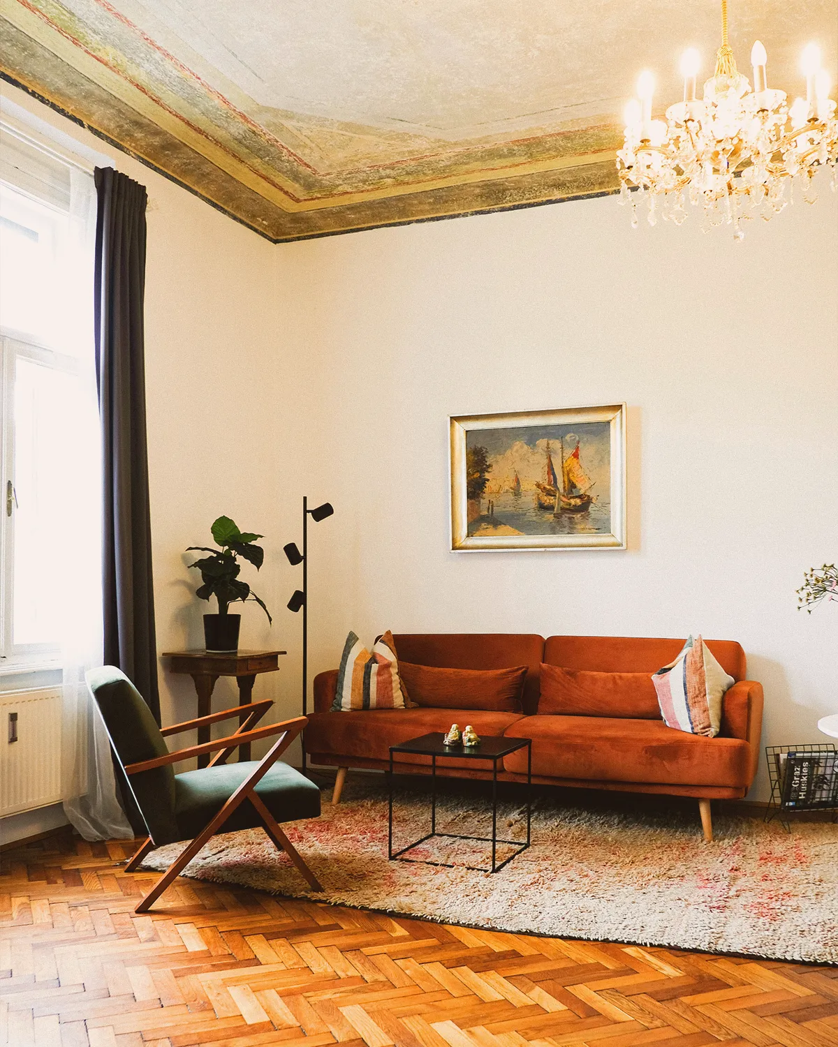 Boutique N°2 • living room with a painted stucco ceiling, a crystal chandelier, a rust-orange sofa and herringbone parquet
