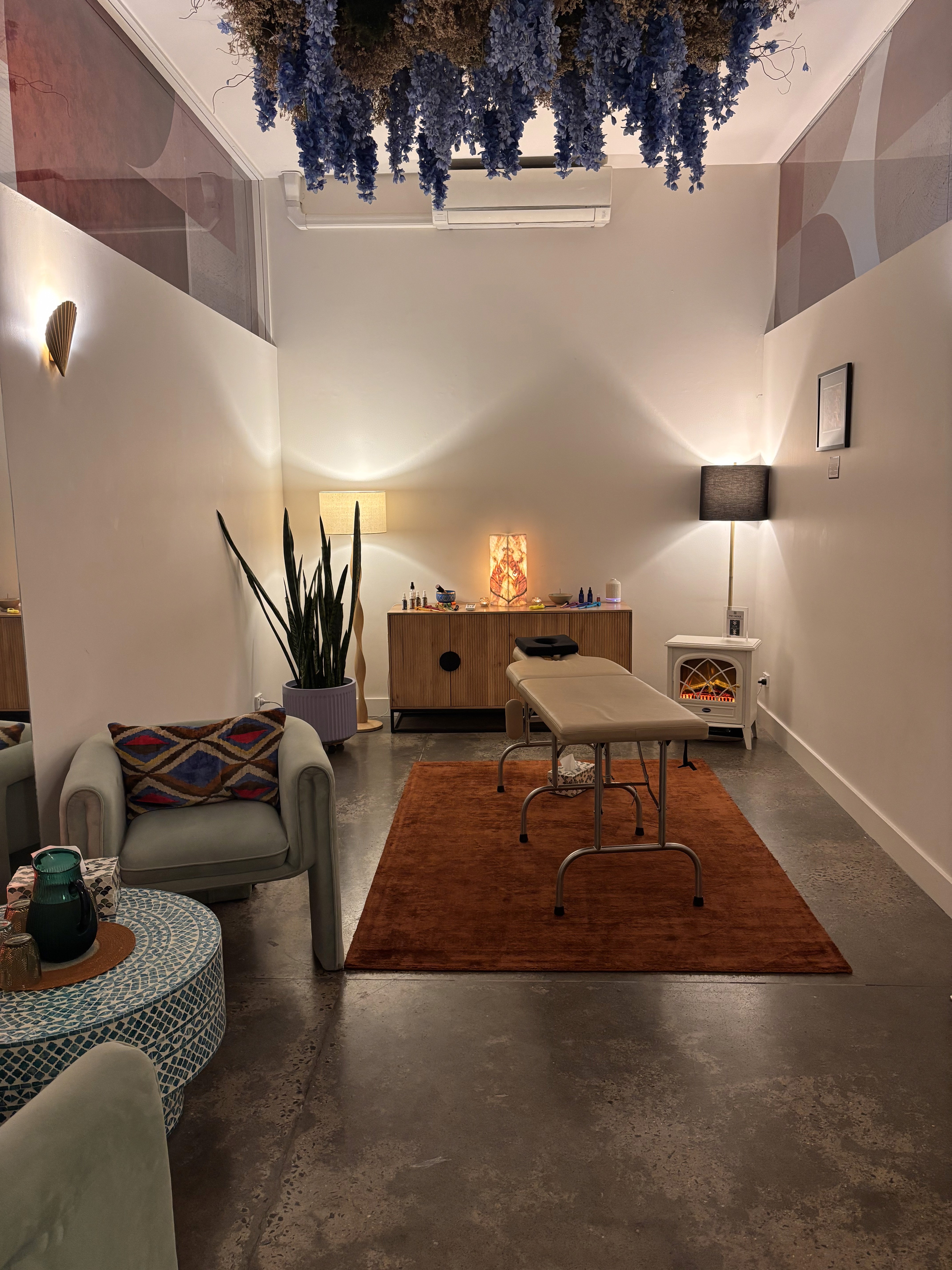 Spinal Energetics HQ client room with orange rug, mosaic table, armchair and blue floral hanging decor