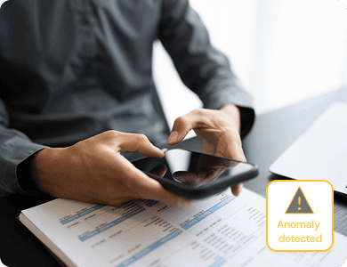 Person reviewing printed financial documents with a yellow alert labelled “Anomaly Detected,” symbolising AI-powered error detection.