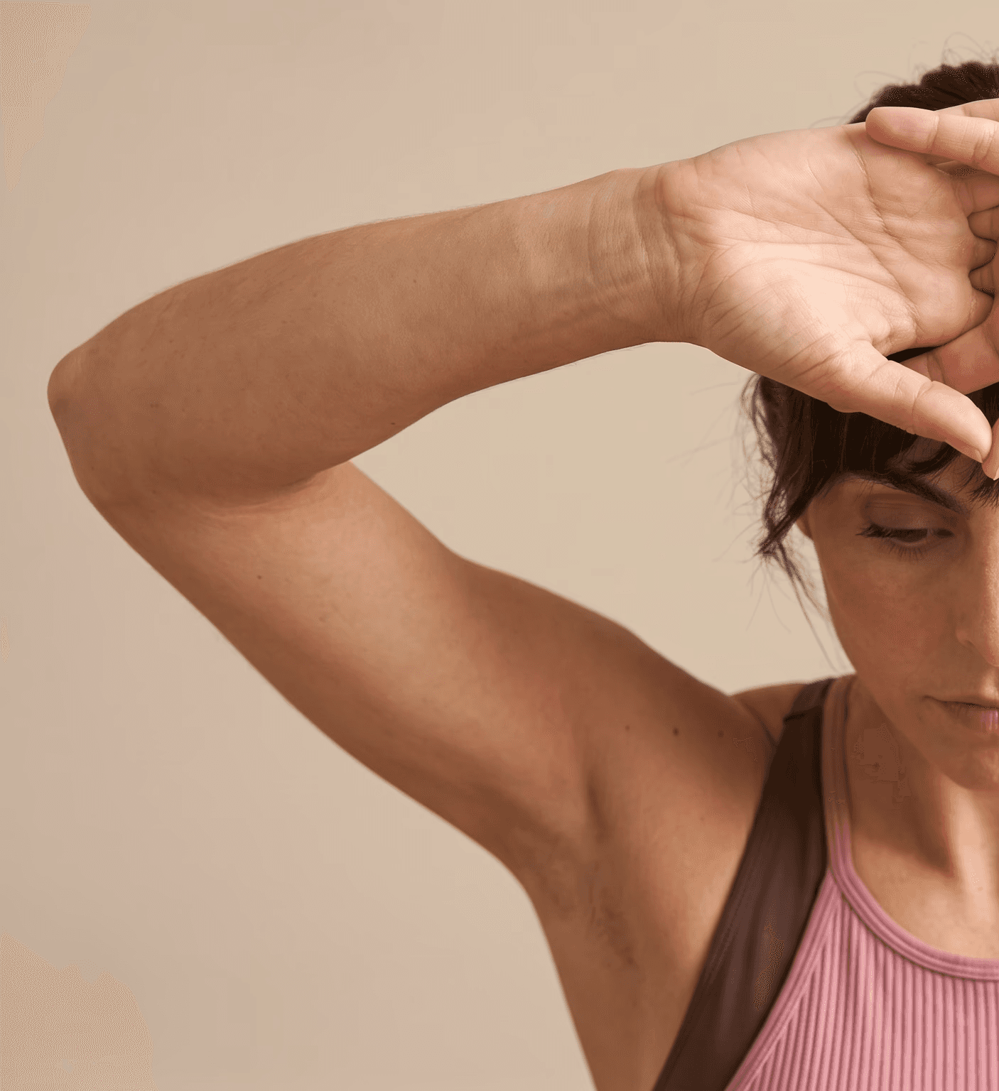Woman in a pink tank top with her hands framing her forehead in a calm, reflective pose