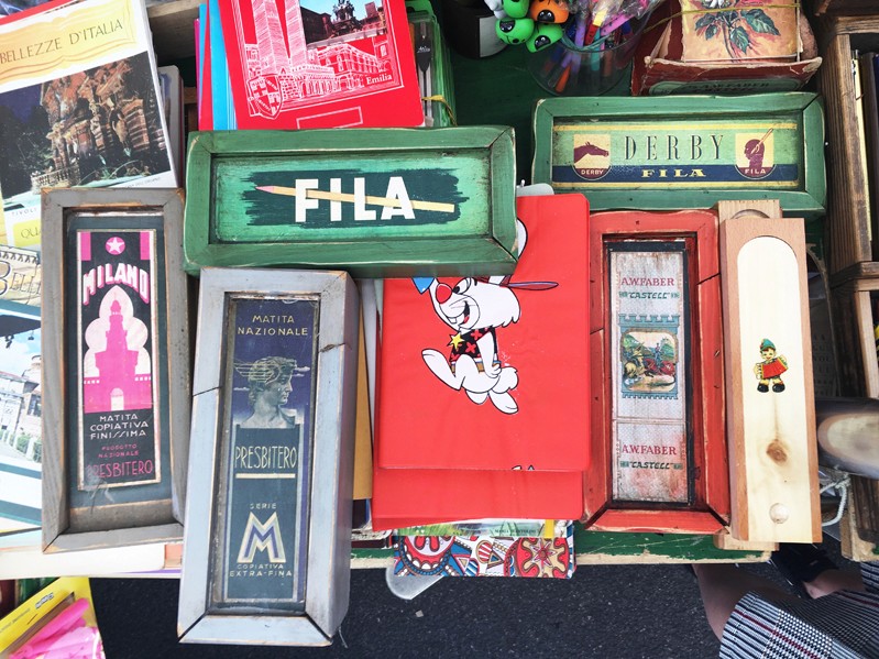 A photo of a set of multiple green, red, grey and brown wood and cardboard crayon boxes with some text and drawings on them.
