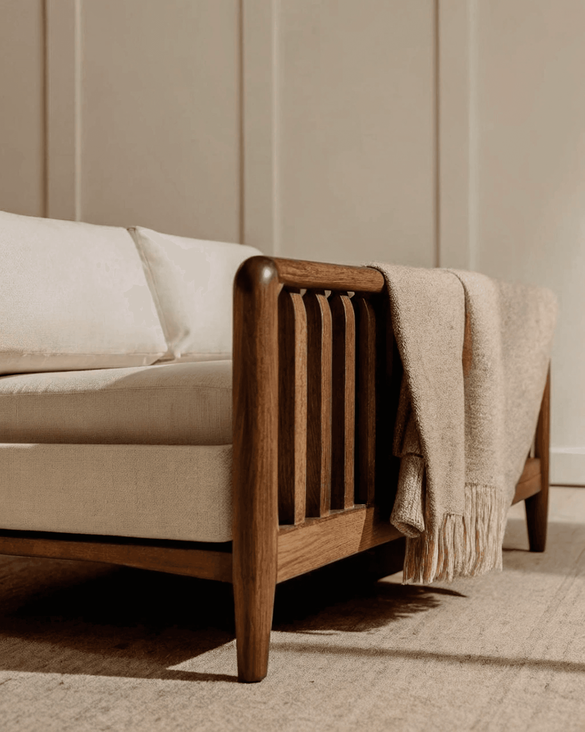 Modern wooden sofa with cream cushions and a beige throw blanket, set against neutral paneling for a cozy, minimalist vibe.
