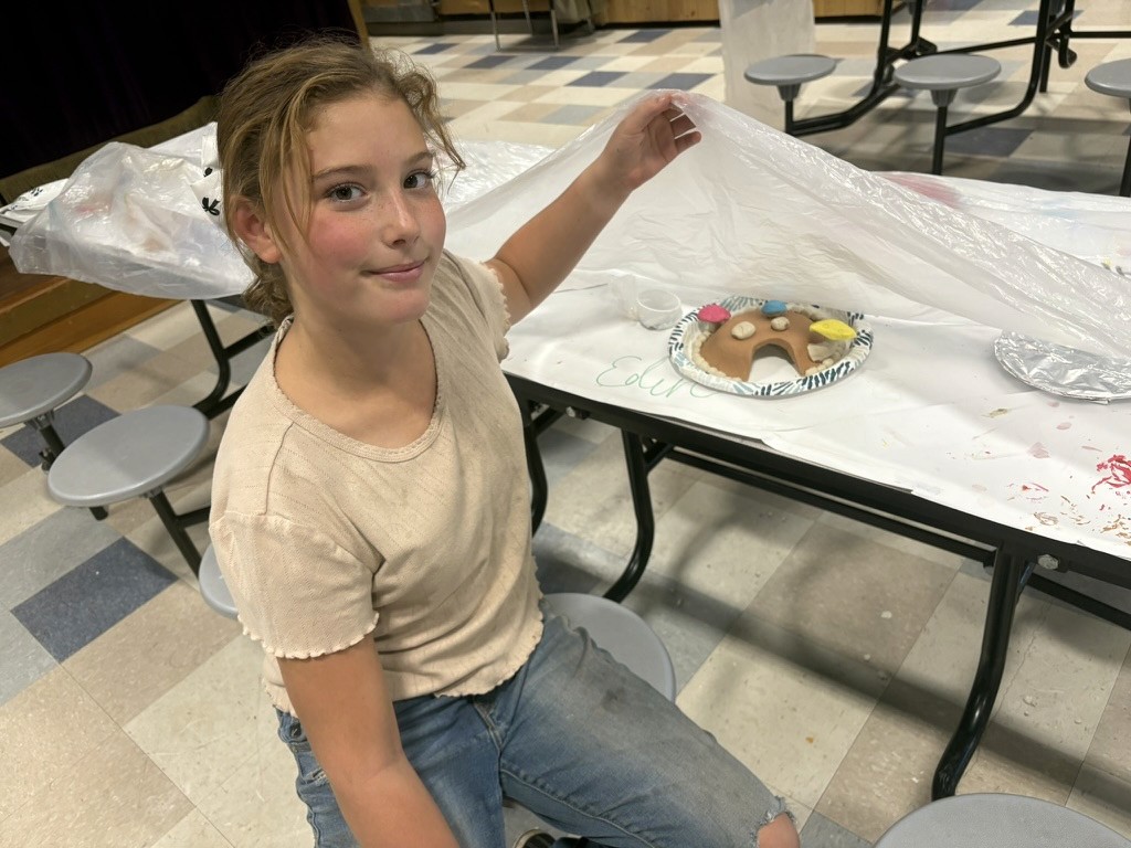 A girl sitting at a table and showing her gnome craft.