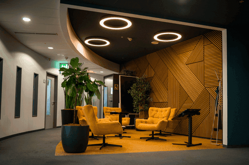 Gemütliche gelbe Sessel auf gelbem Teppich vor einer Wand mit geometrischem Holzpaneelmuster und runden Deckenleuchten