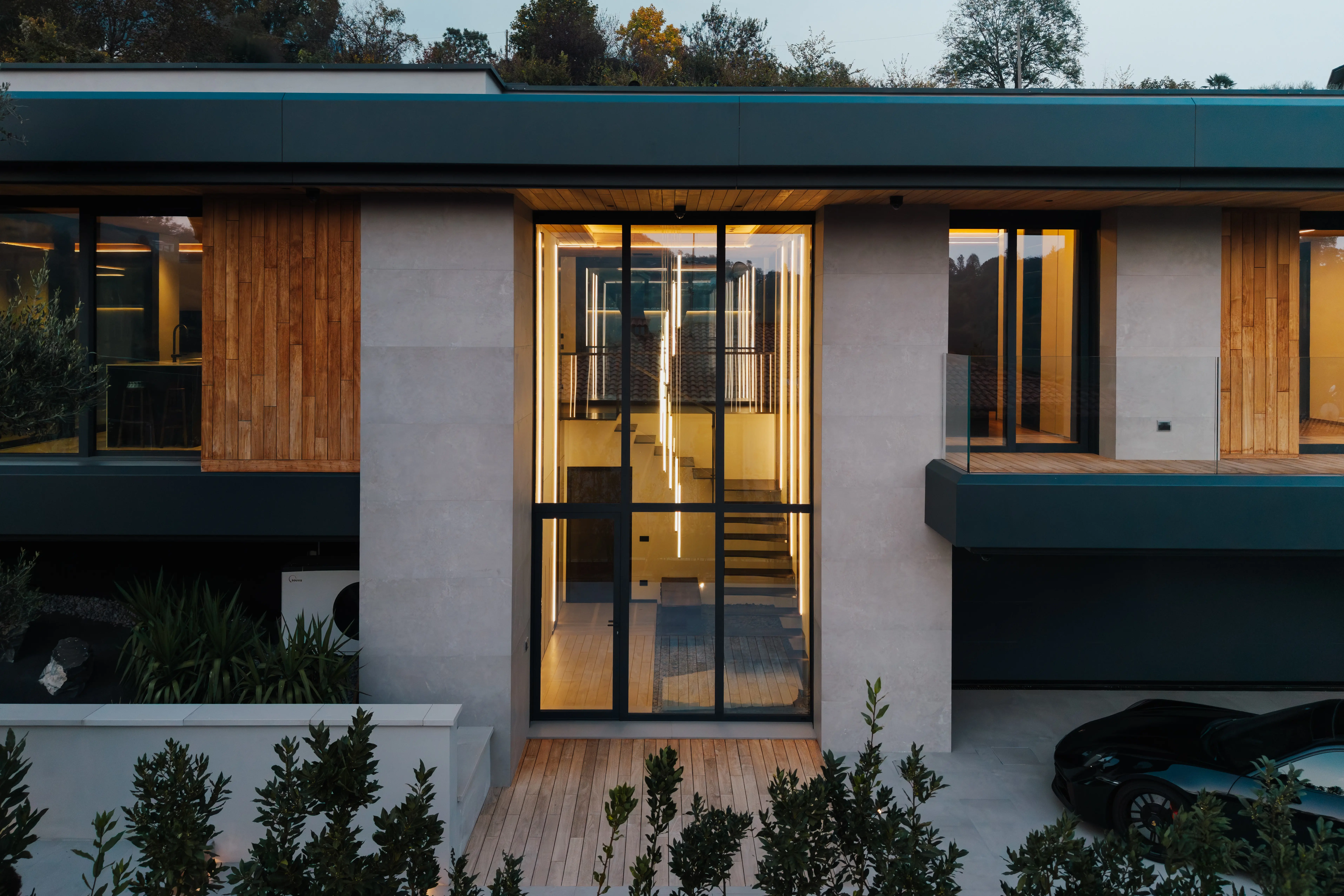 Close-up of a modern building facade featuring vertical wooden panels and black-framed windows, with natural light casting tree shadows on the surfaces.