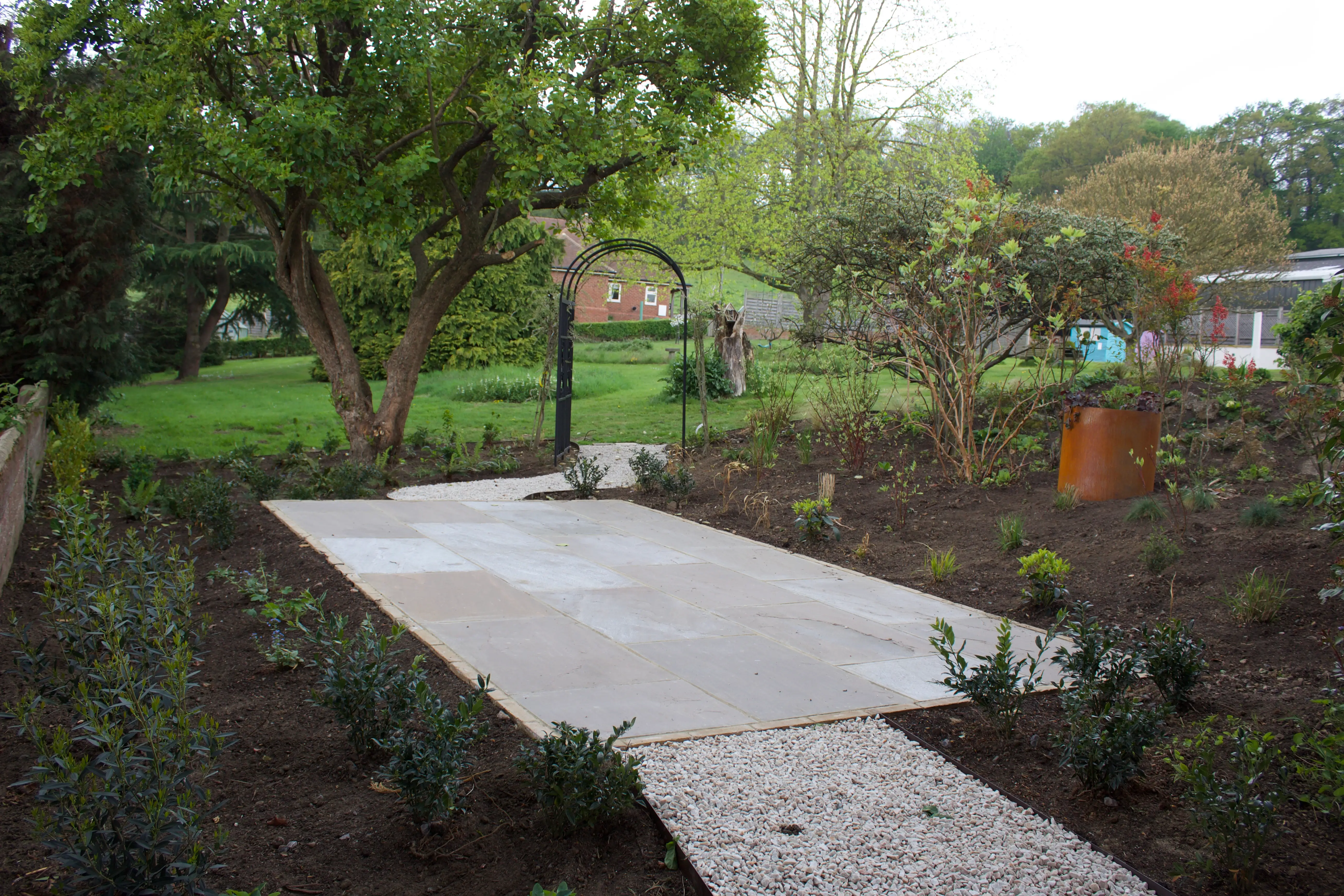 A pathway made of concrete slices surrounded by grass and plants, leading to a green area in the background.