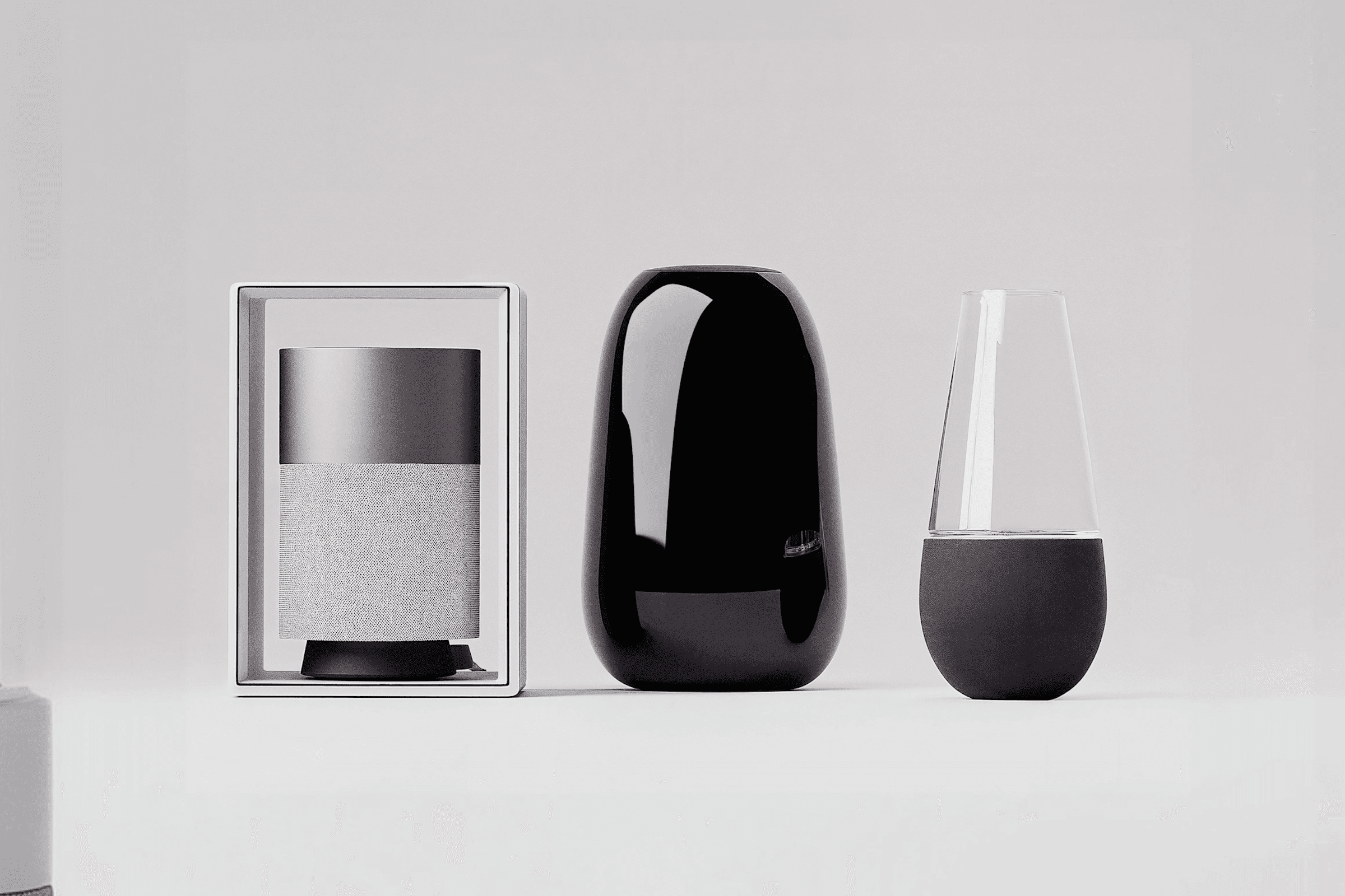 Three modern, minimalist objects: a framed speaker, a glossy black vase, and a conical glass piece with a black base.