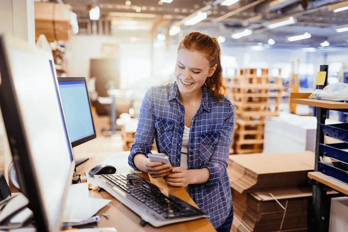 Smiling warehouse worker using smartphone at desk