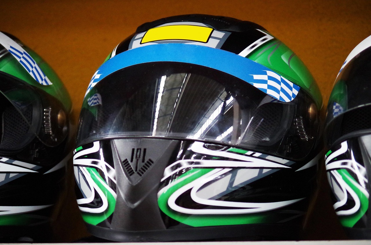 A young person with curly hair smiles at the camera while sitting in front of a laptop against a dark background.