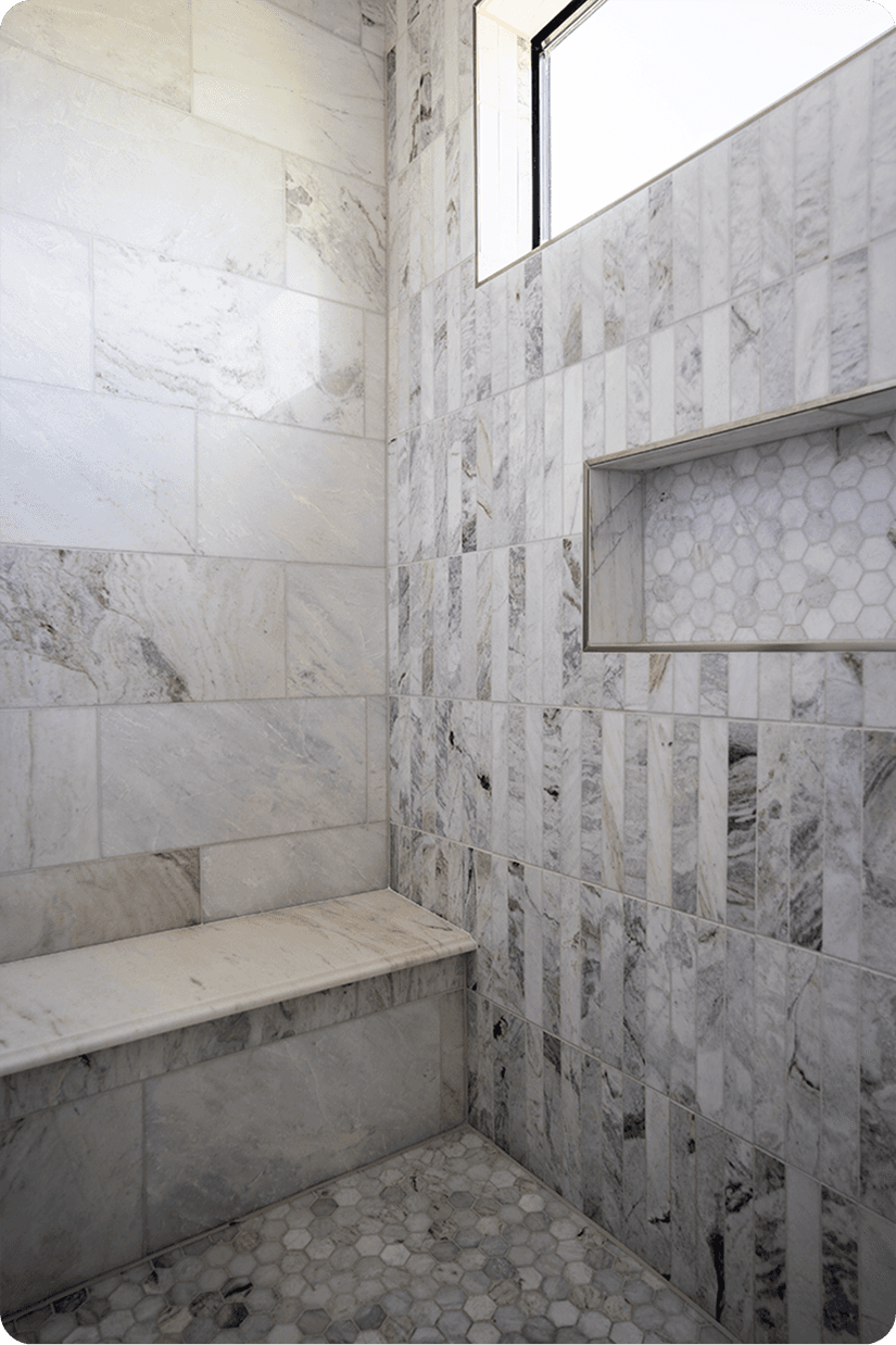 Luxurious marble shower with built-in niche, hexagon mosaic floor tiles, and natural light from Floor & Decor
