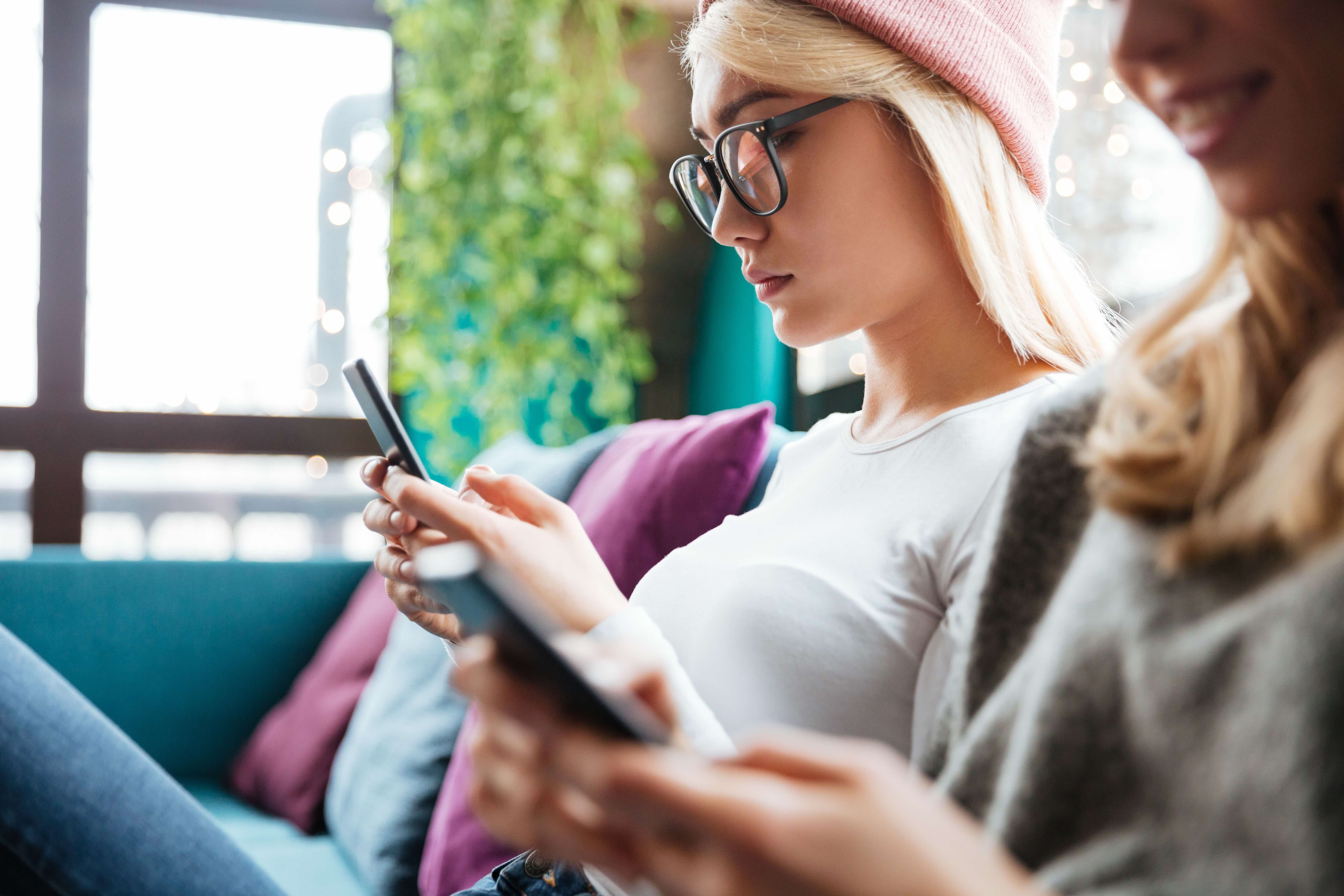 Frau sitzt auf dem Sofa und schaut in ihr Handy