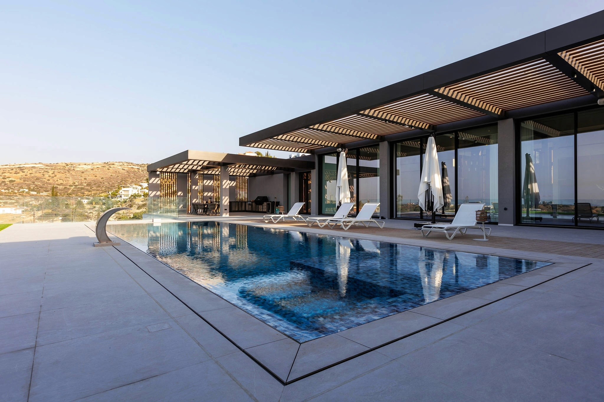 Villa Trio pool terrace with pergola shading, sun loungers, and full-height glazing