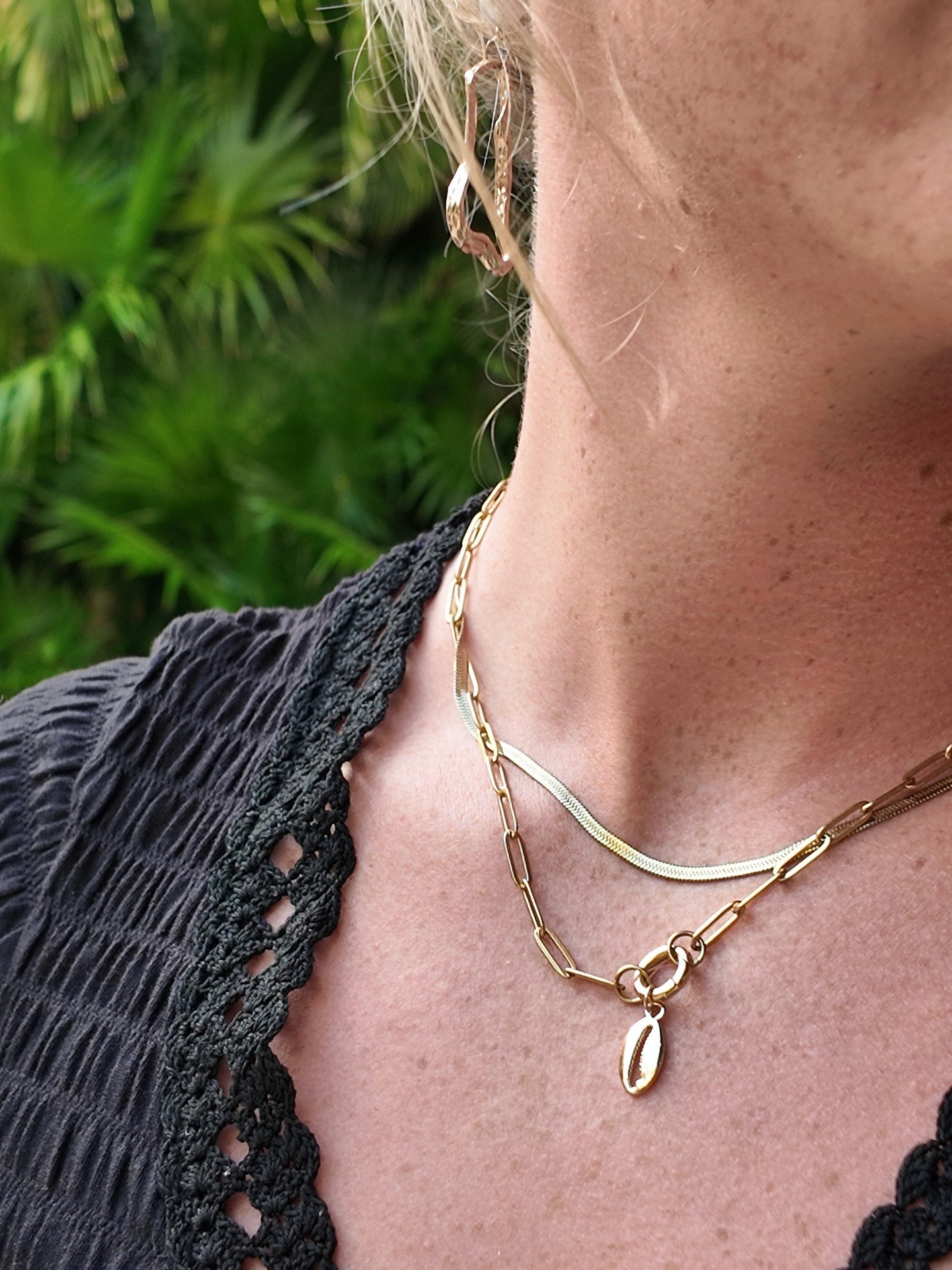 Smiling man wearing a turquoise t-shirt and white overshirt, confidently adjusting his collar against a teal-blue studio backdrop.