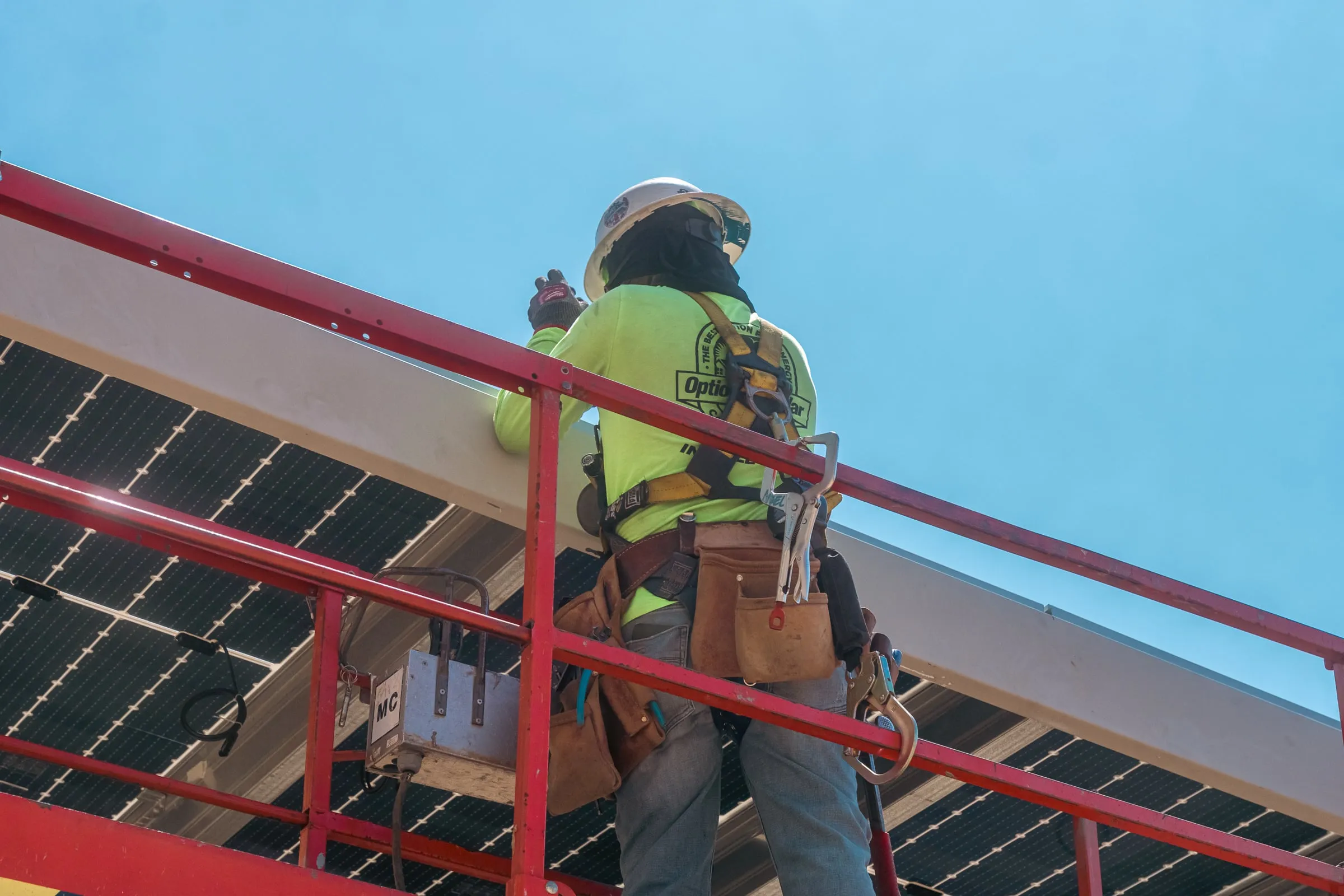 An installer in a high-visibility vest working from a raised lift beside a solar carport canopy