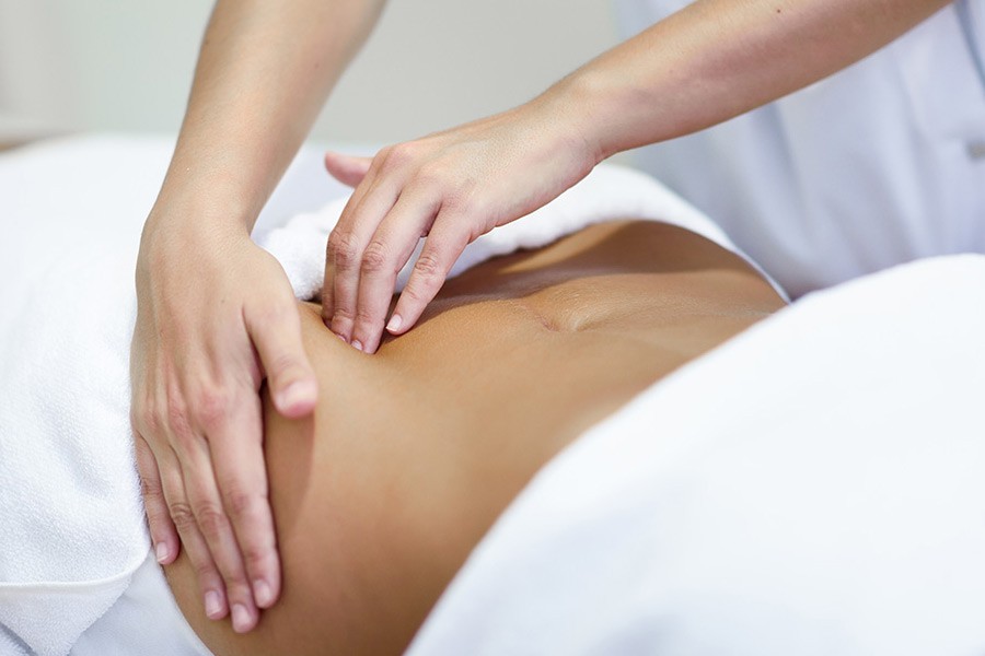 A woman lying down with a towel wrapped around her head, her face glowing with facial oil. She has a peaceful expression, enjoying a skincare treatment.