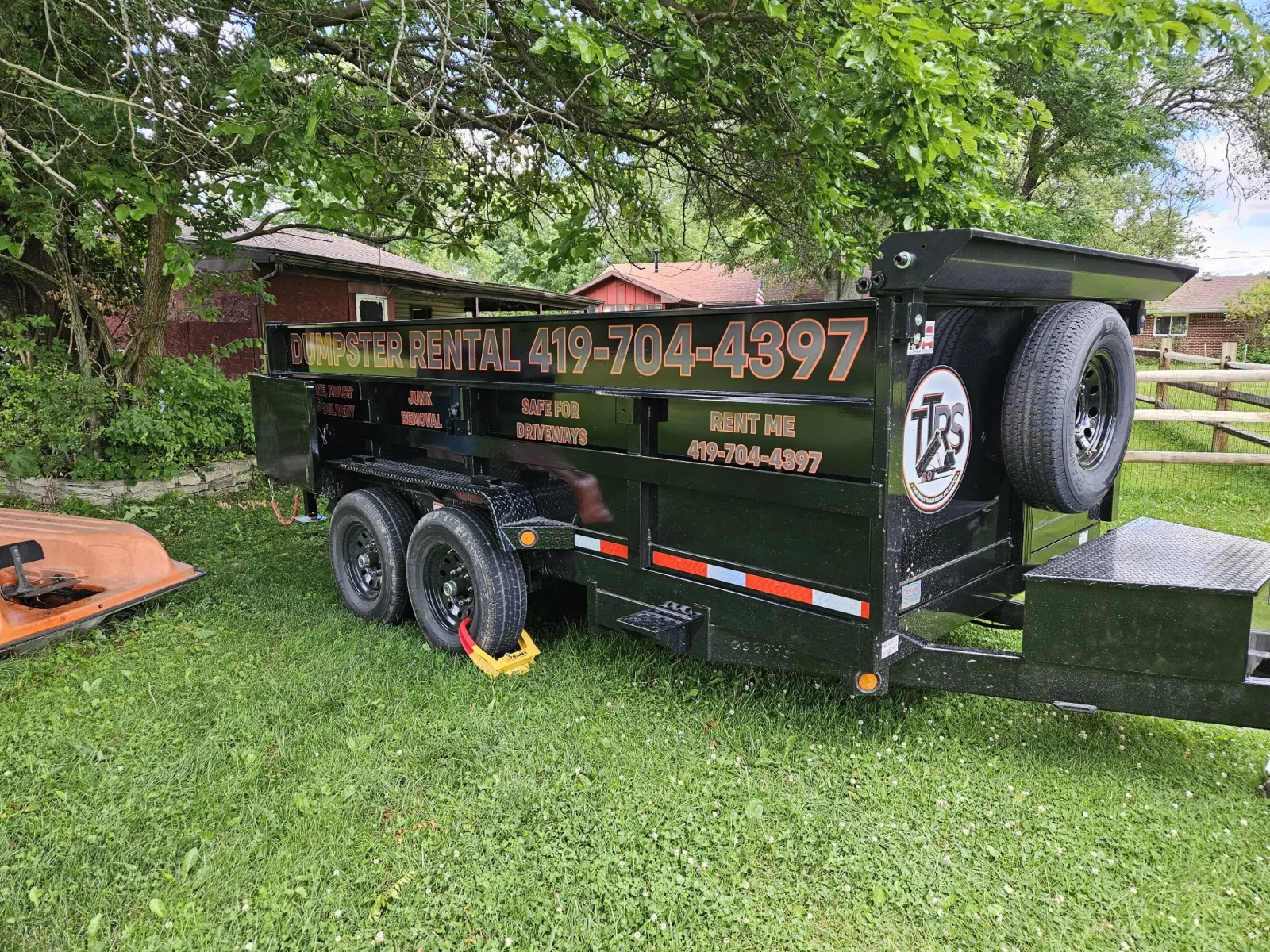 Temperance Trailer Rentals black dump trailer parked in a grassy backyard for a yard cleanup