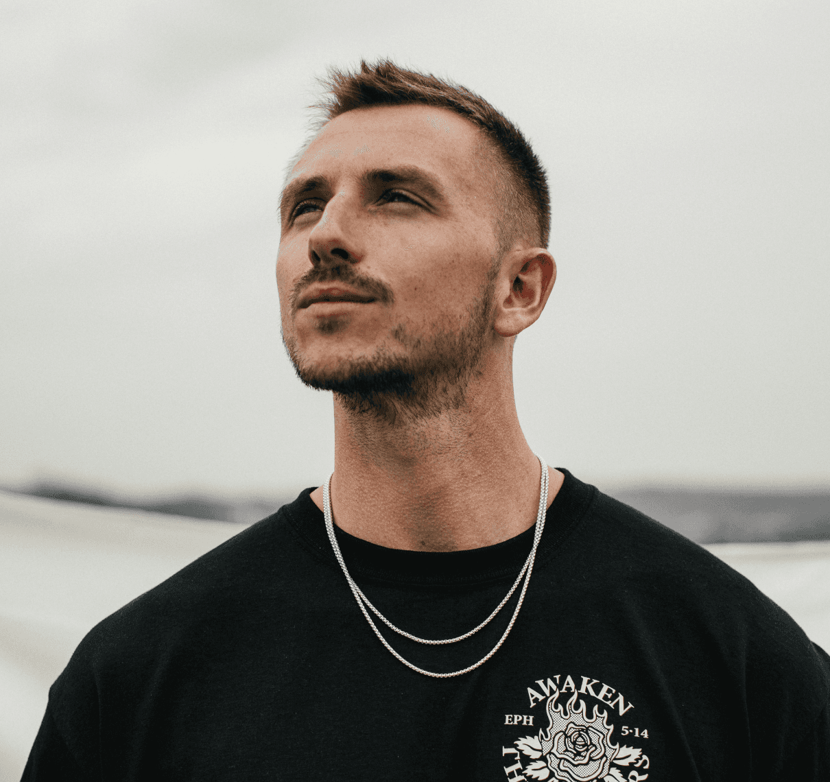 Man with brown hair wearing a black T-shirt, looking upward