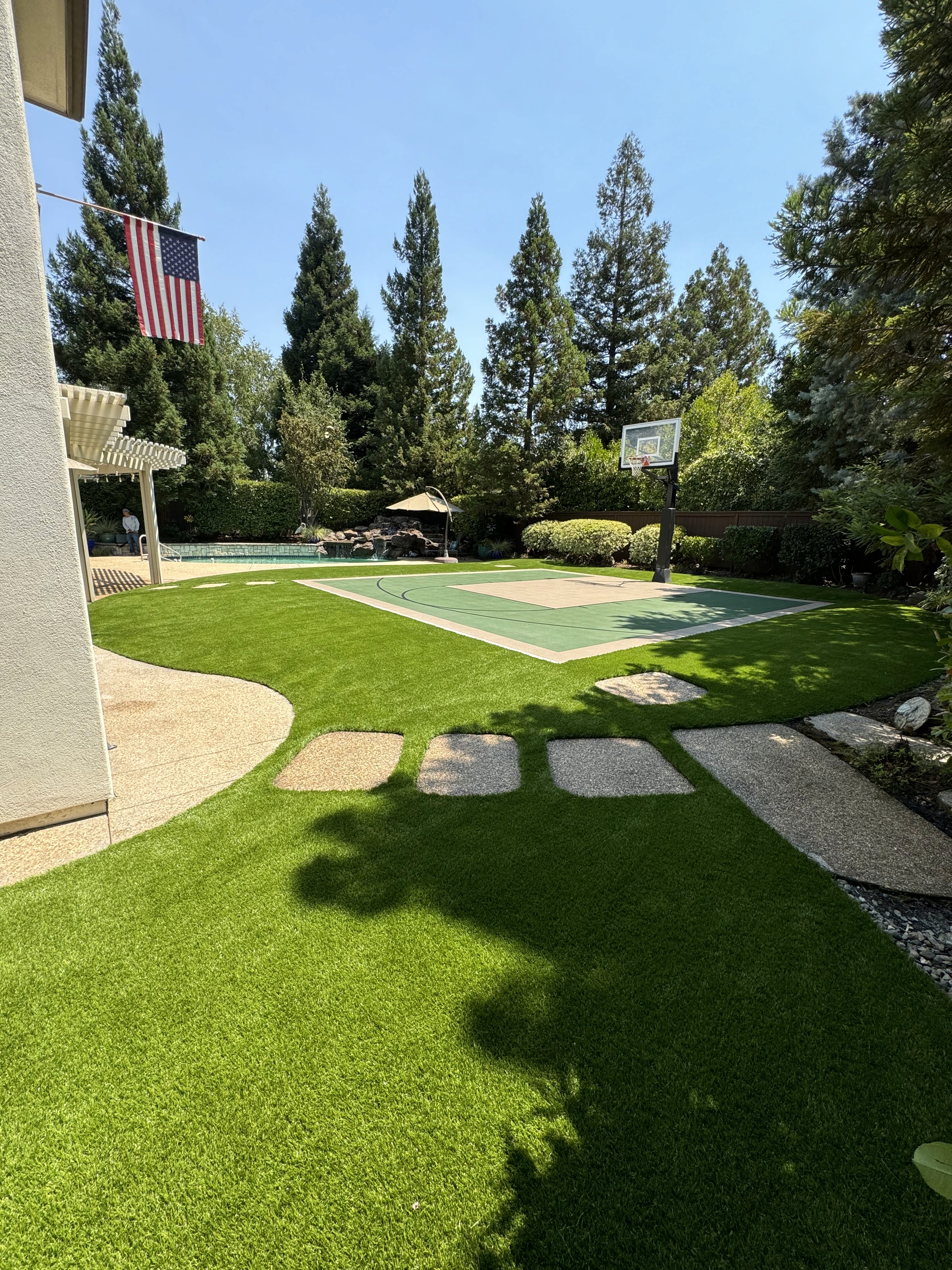 Artificial turf backyard with a sport court, basketball hoop, and stepping stones.