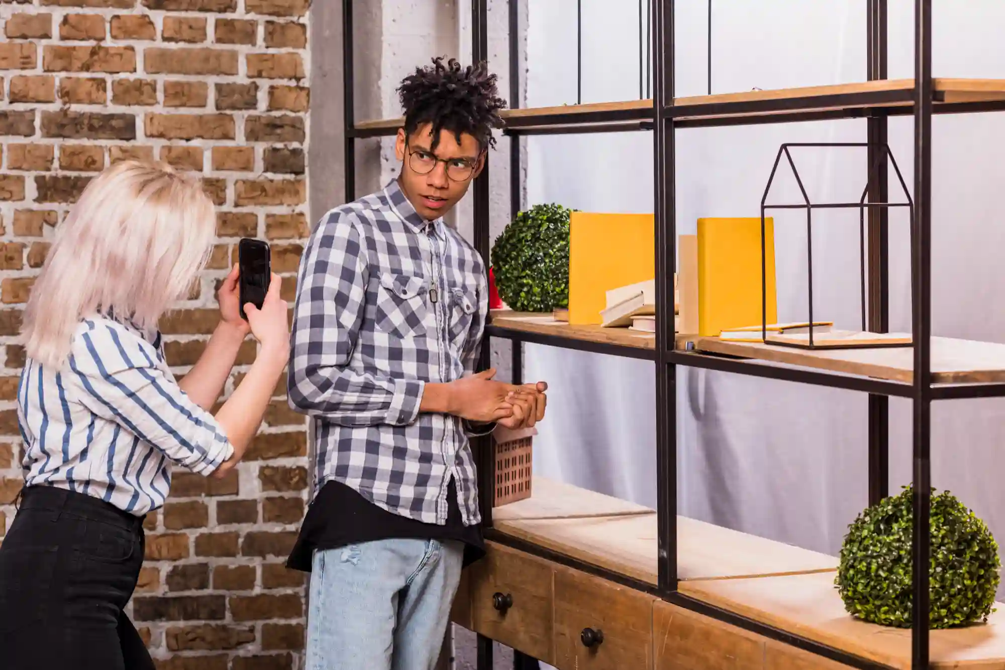 A woman takes a photo of a man in front of a shelf.