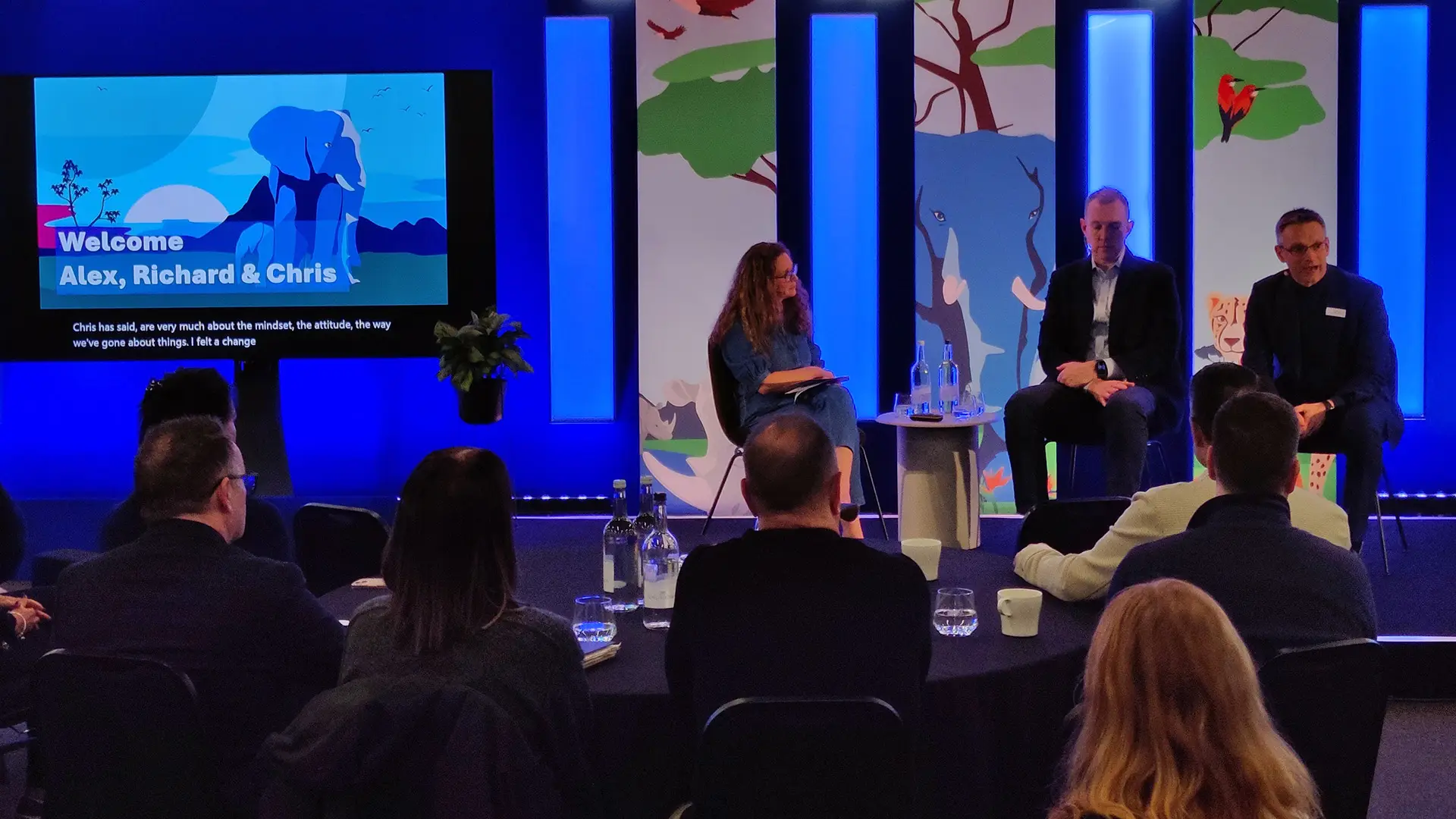 Panel discussion at a Bupa Strategy Cascades event, with speakers seated on stage in front of illustrated animal-themed panels and a screen welcoming senior leaders.