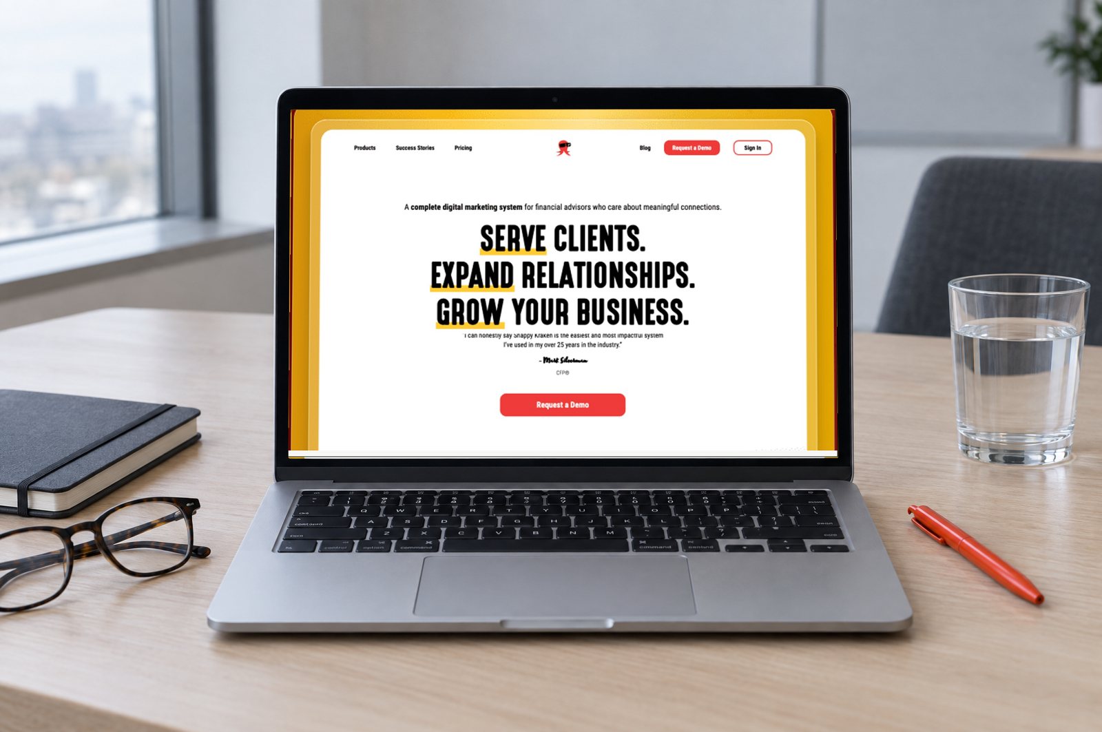A laptop on a meeting-room table showing the real Snappy Kraken homepage built in HubSpot by Demand Designer: 'Serve clients. Expand relationships. Grow your business.' with a Request a Demo button