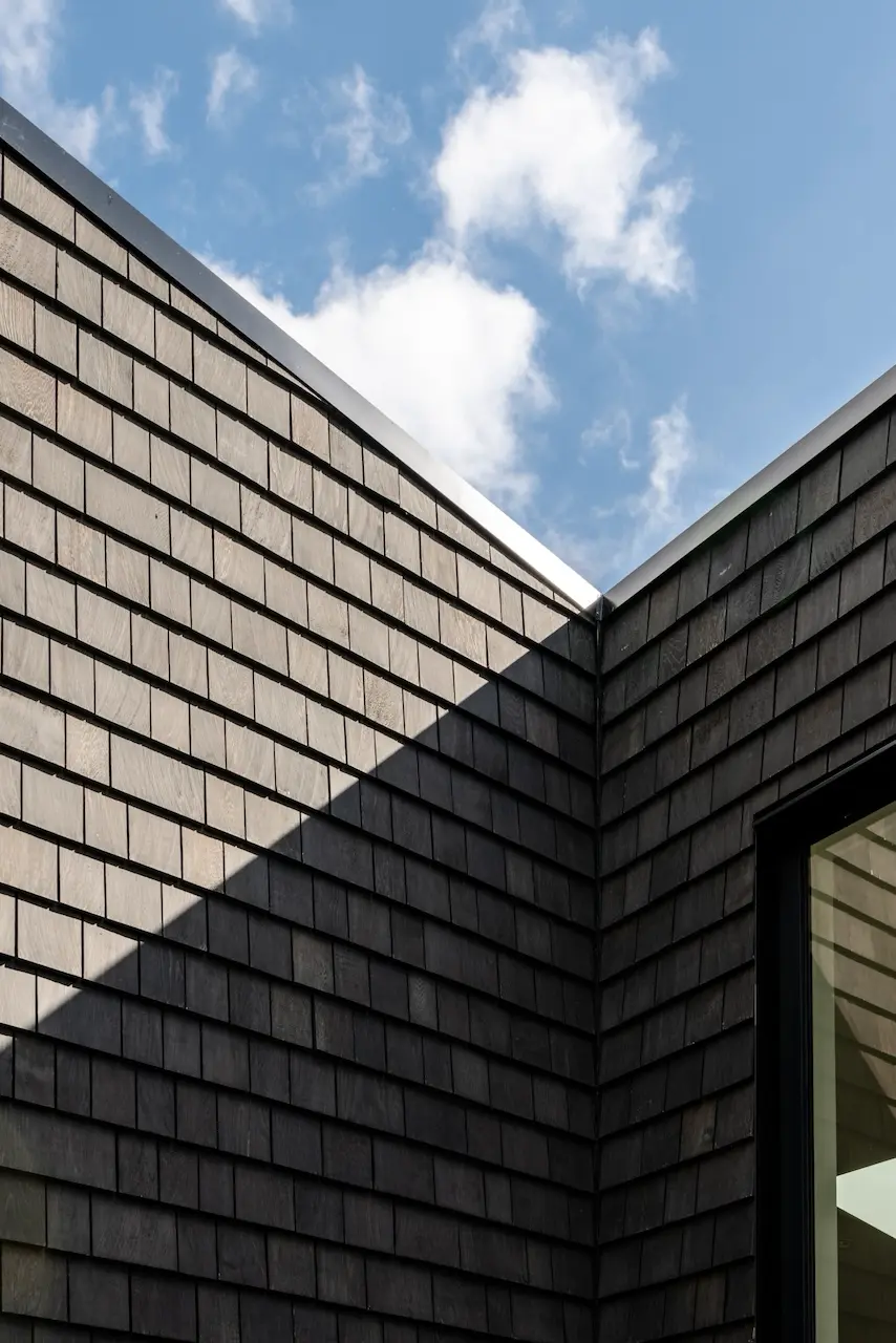 Modern two-story home with large glass windows, warmly lit interiors, and a balcony. Surrounded by trees and a manicured lawn at dusk. Cozy ambiance.