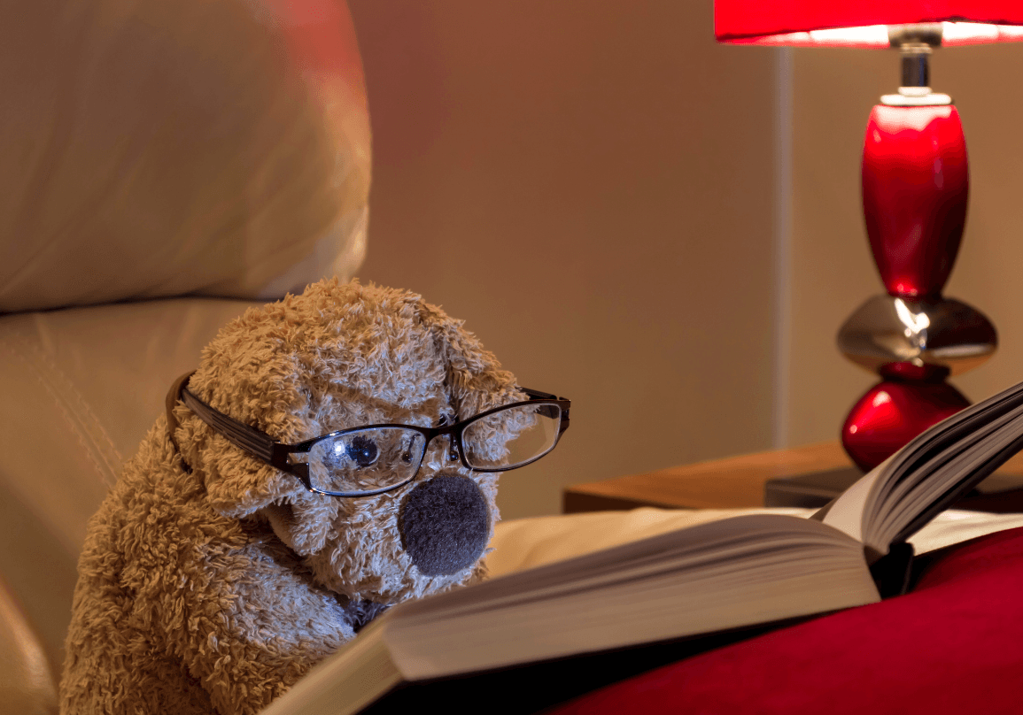 A bear with glasses on reading a book by lamplight