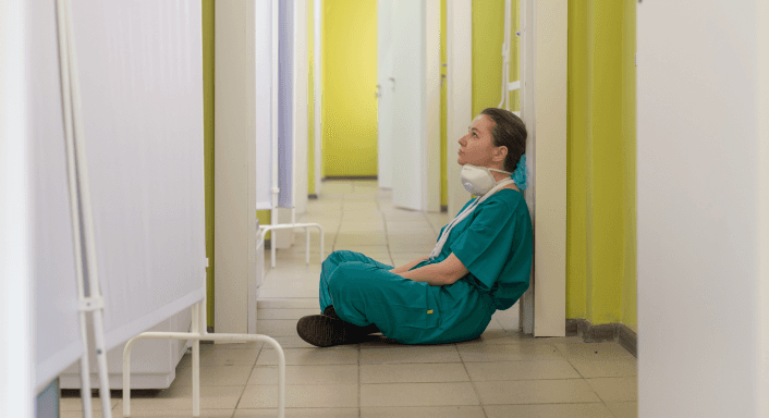 Exhausted healthcare worker sitting on a hospital corridor floor.