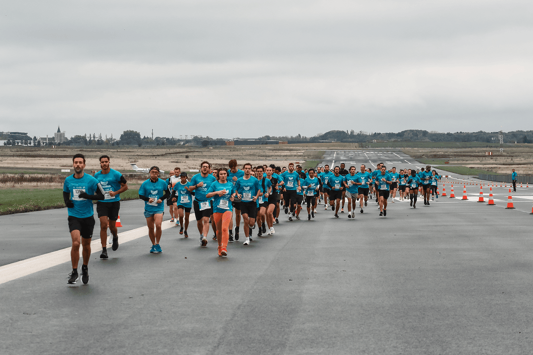 Coureurs vêtus de t-shirts bleus participant à un événement sportif sur une piste d'atterrissage, avec des cônes de signalisation alignés.