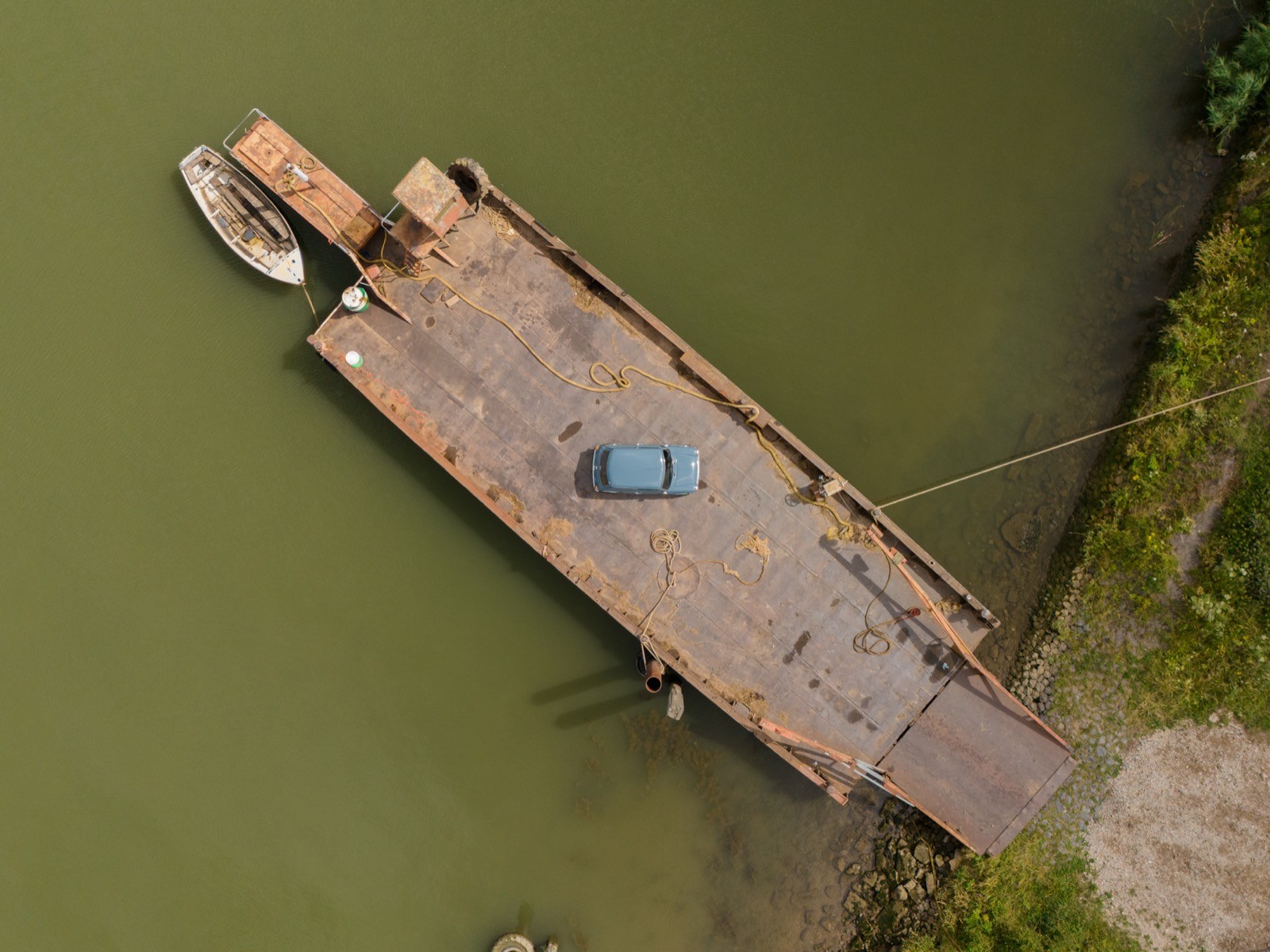 Aerial view of a wooden dock extending into a calm green water body, surrounded by lush greenery.