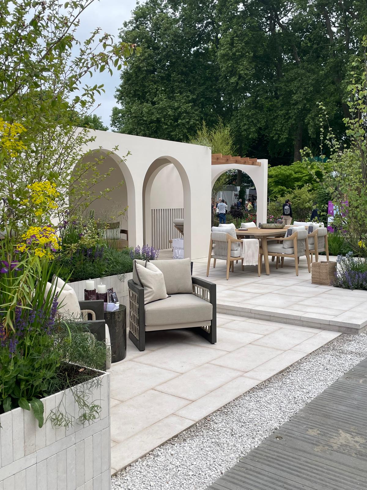 A serene outdoor seating area with archways, surrounded by greenery and paved pathways.